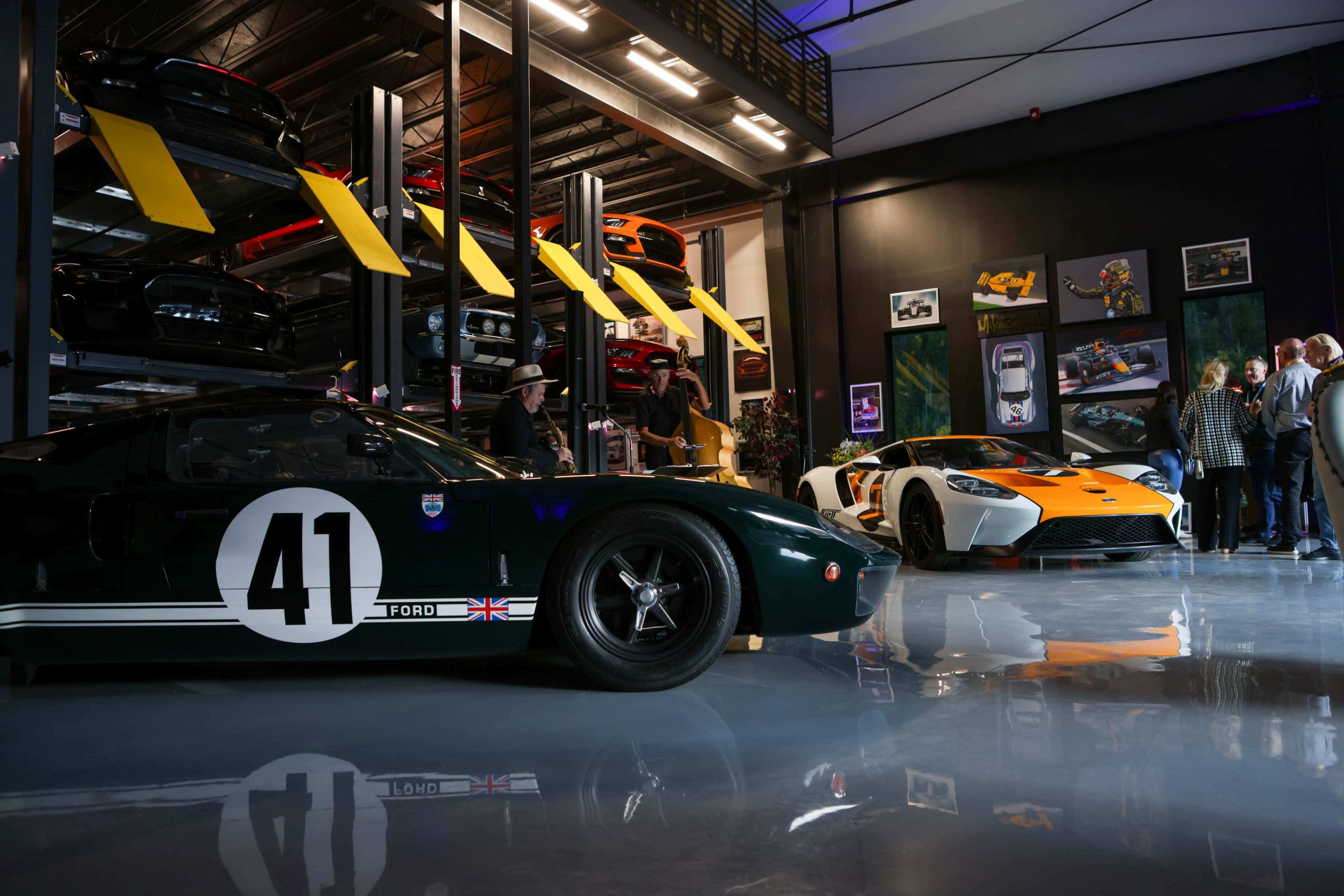 A vintage green race car with the number 41 is parked beside a modern orange and white sports car in a well-lit garage filled with various cars.
