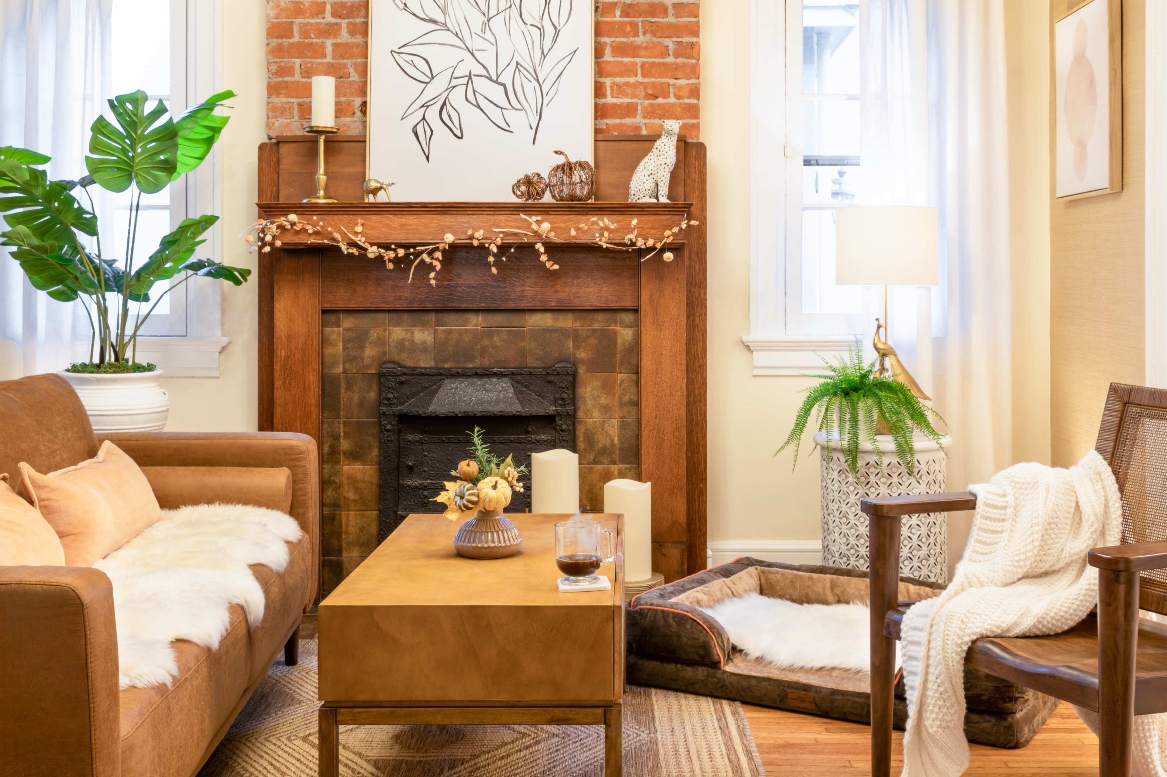 The living room features a brown leather sofa and an armchair positioned around a wooden coffee table, with a fireplace adorned with decorative elements and a large houseplant nearby.
