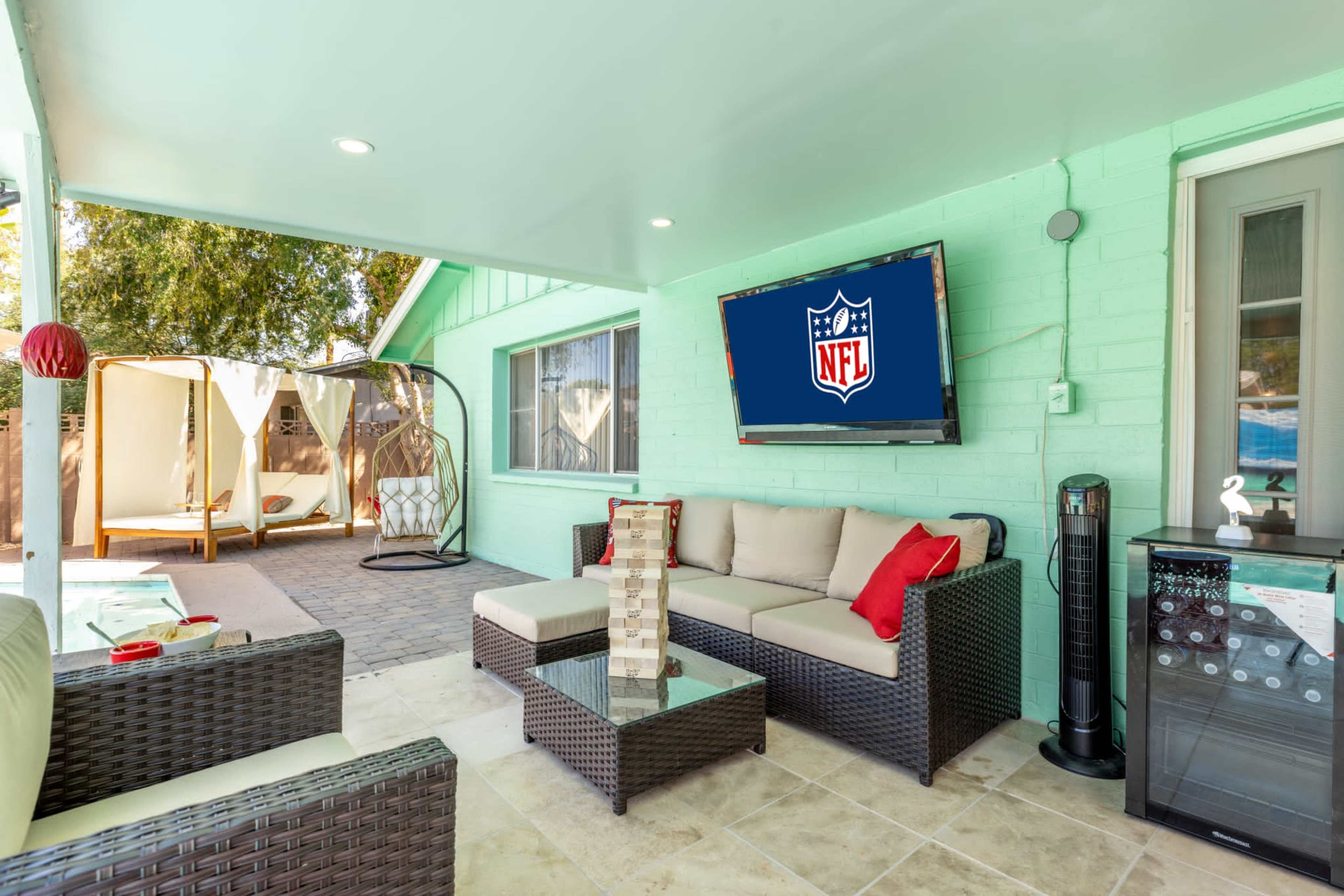 A covered patio features a seating area with a television displaying the NFL logo, surrounded by a modern outdoor setting.
