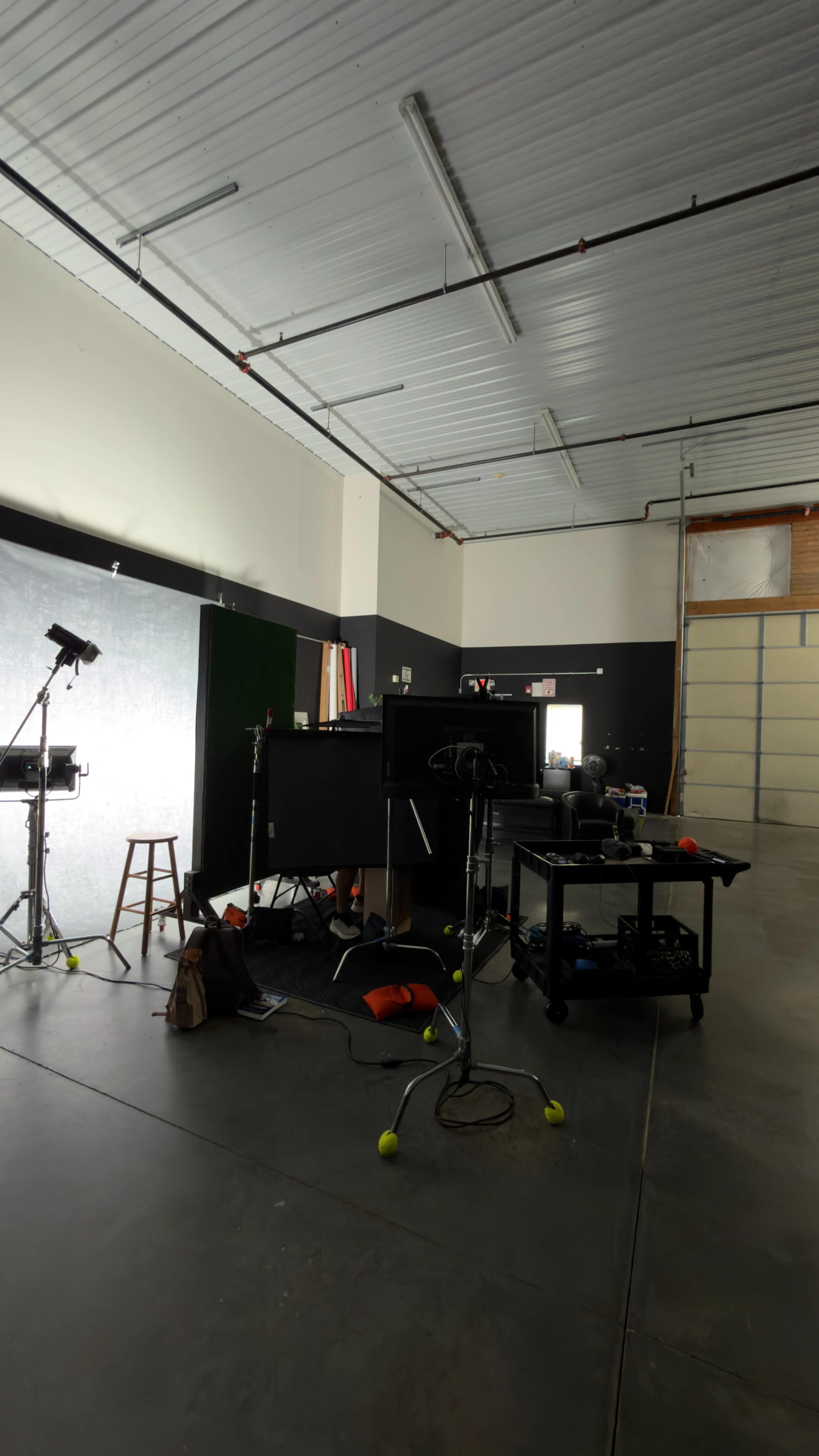 The image shows a photography studio with various equipment, including lights, cameras, a stool, a table, and a large backdrop.