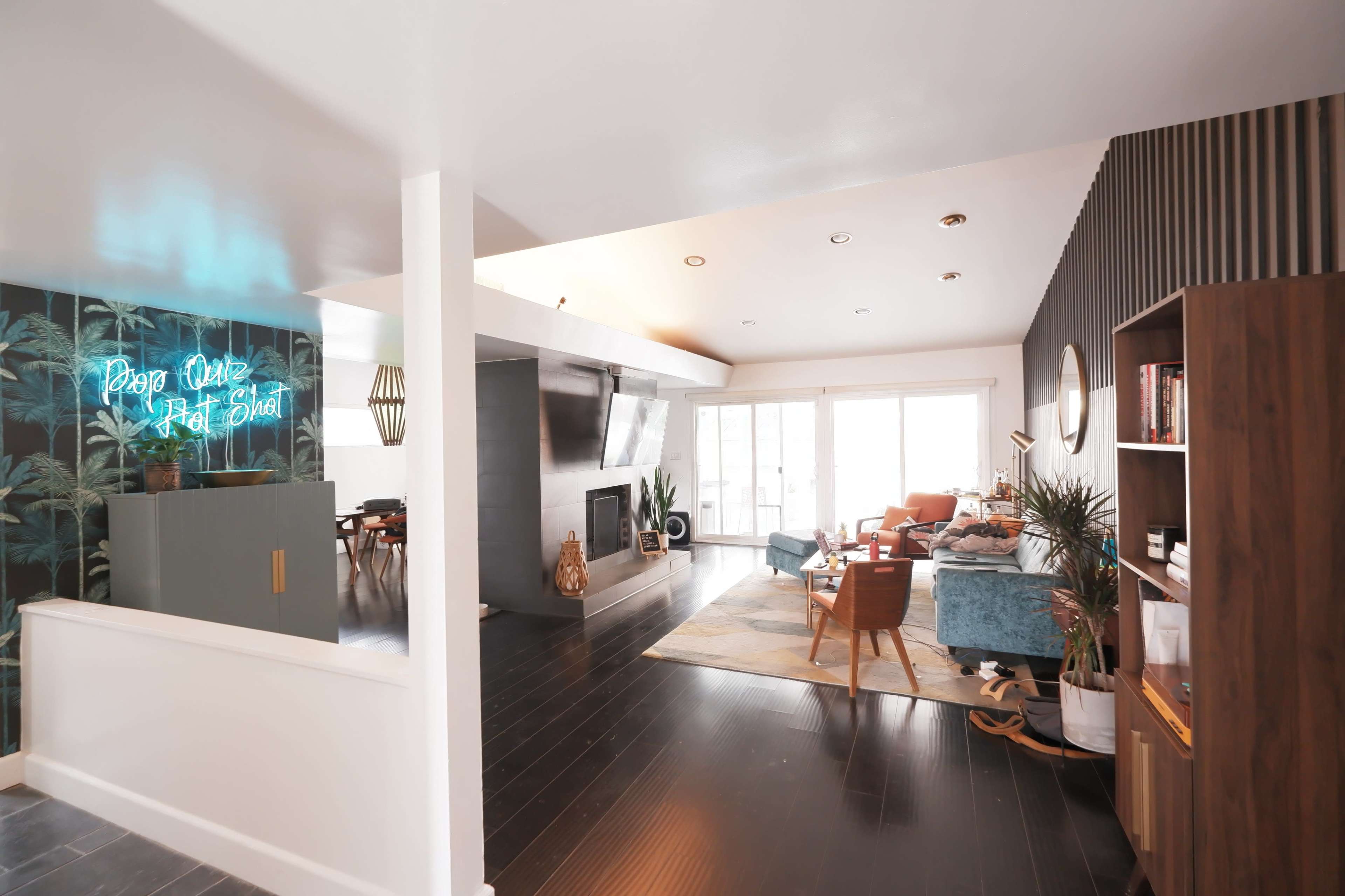 A modern, open-concept living space featuring a blue sofa, a television mounted on the wall, and a bright area with large windows leading to a patio.