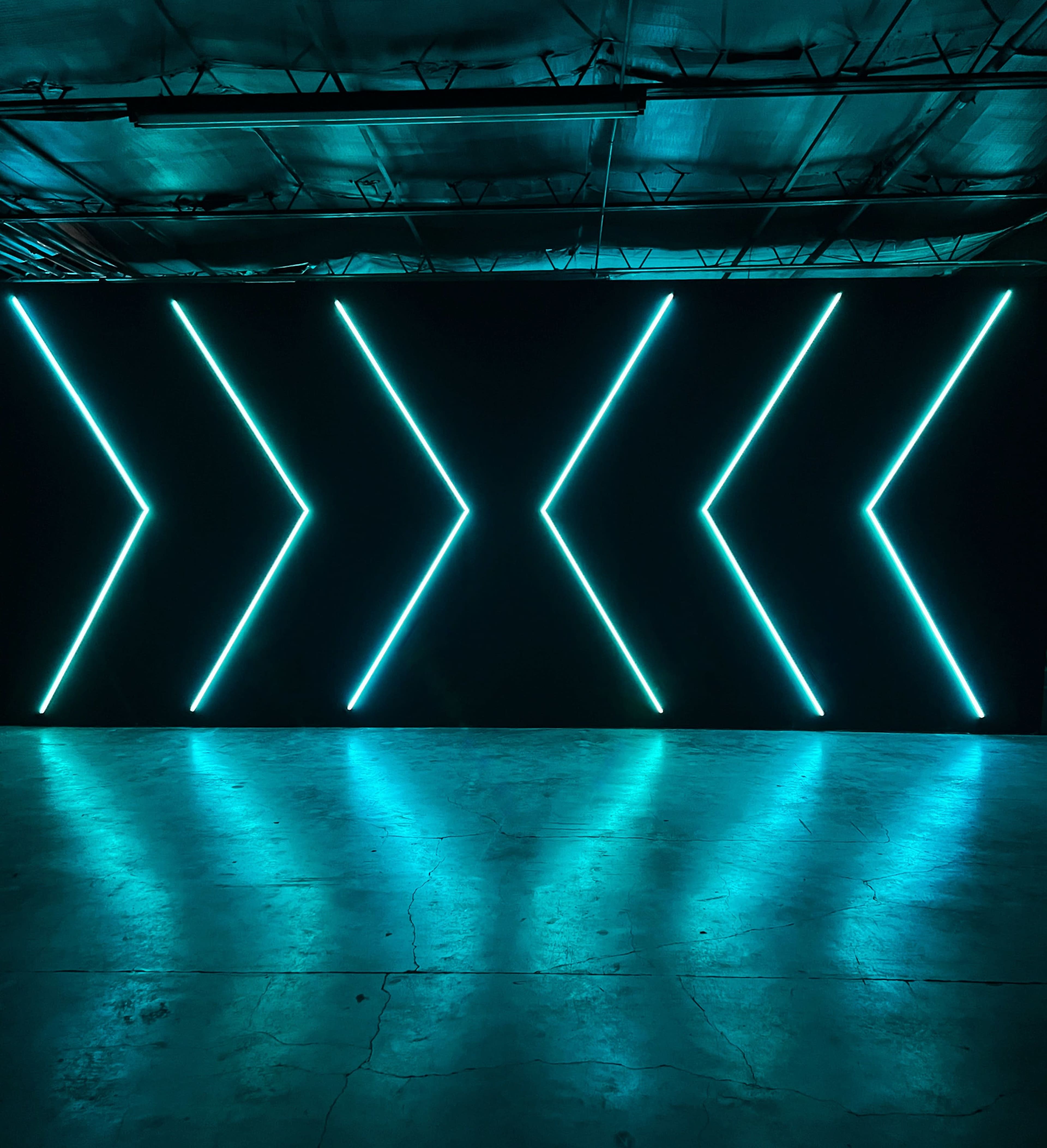 A dark room with a wall featuring bright, linear neon light arrows arranged in a pattern.