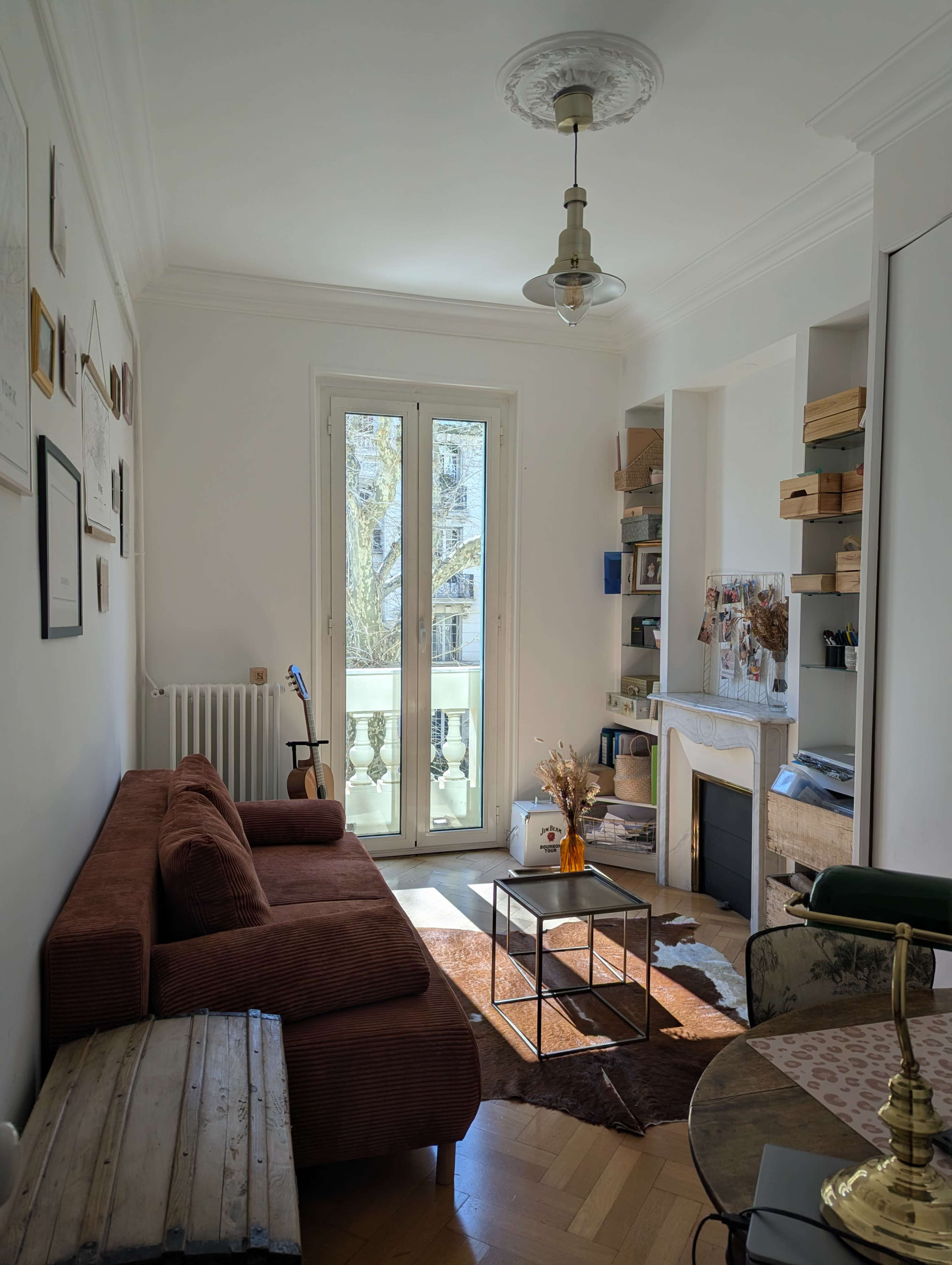 The room features a brown sectional sofa, a coffee table, and a decorative fireplace, with large windows allowing natural light to enter.