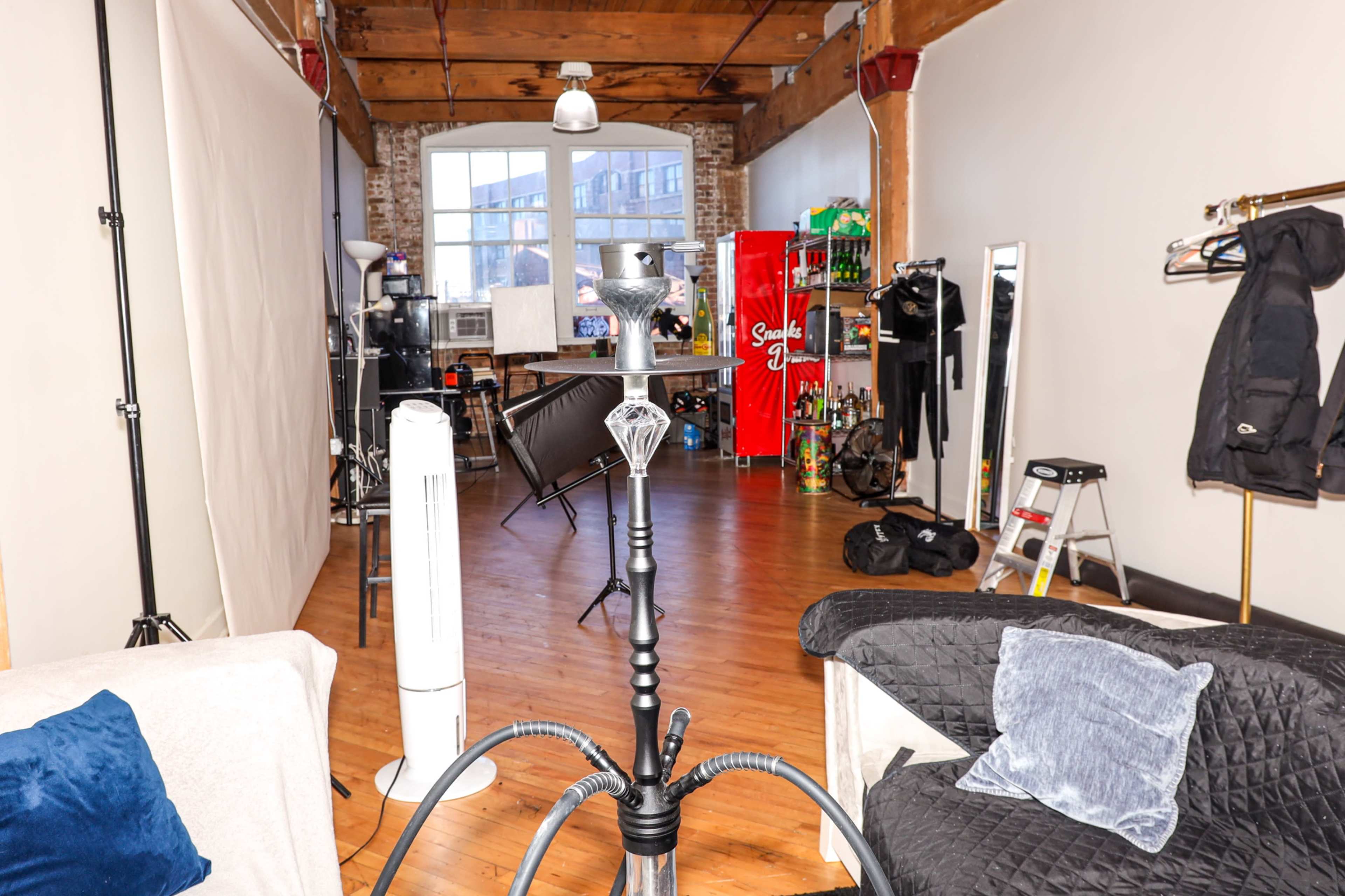 The image shows a spacious, vacant studio or event space with wooden floors, exposed brick walls, and various furniture and equipment along the sides.