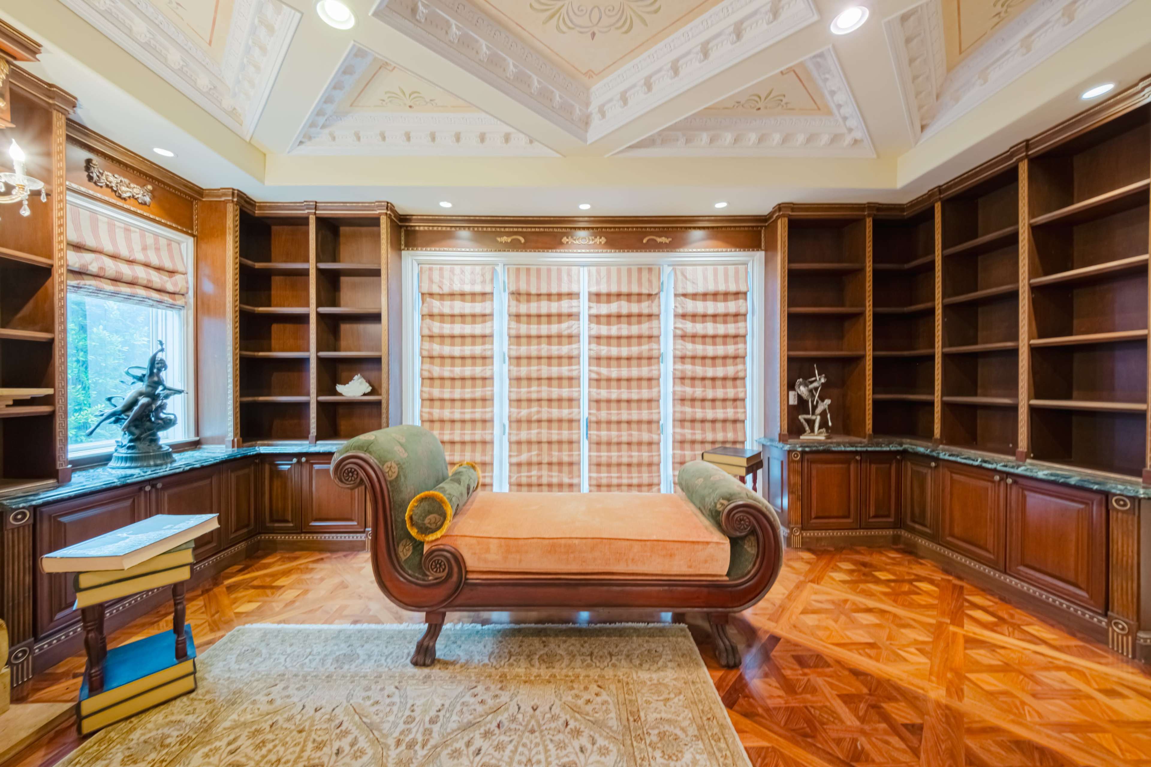 A spacious room with wooden bookshelves, an ornate ceiling, and a chaise lounge in the center.