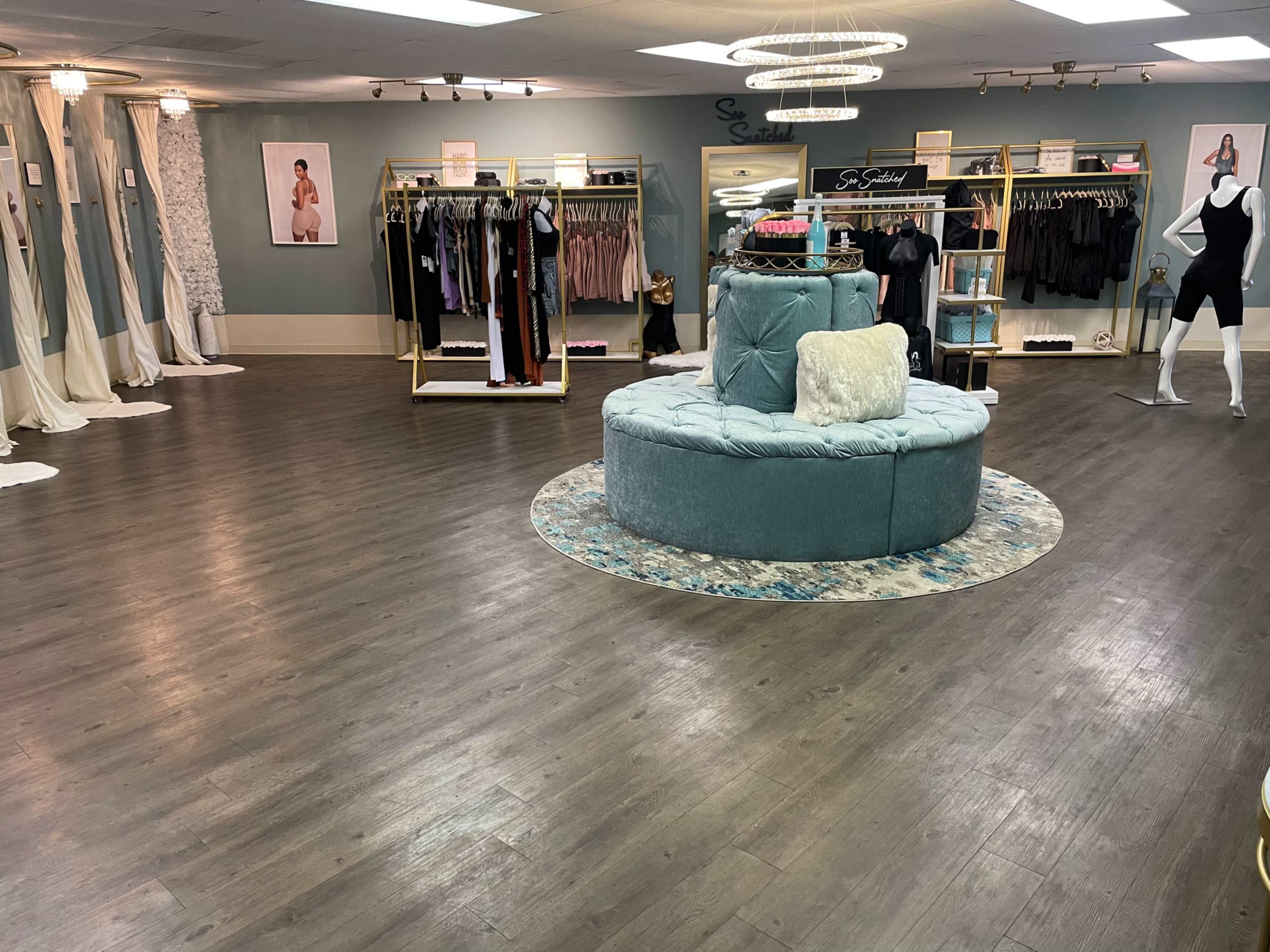 The image shows a spacious boutique with racks of clothing and a central circular seating area, featuring soft lighting and elegant decor.