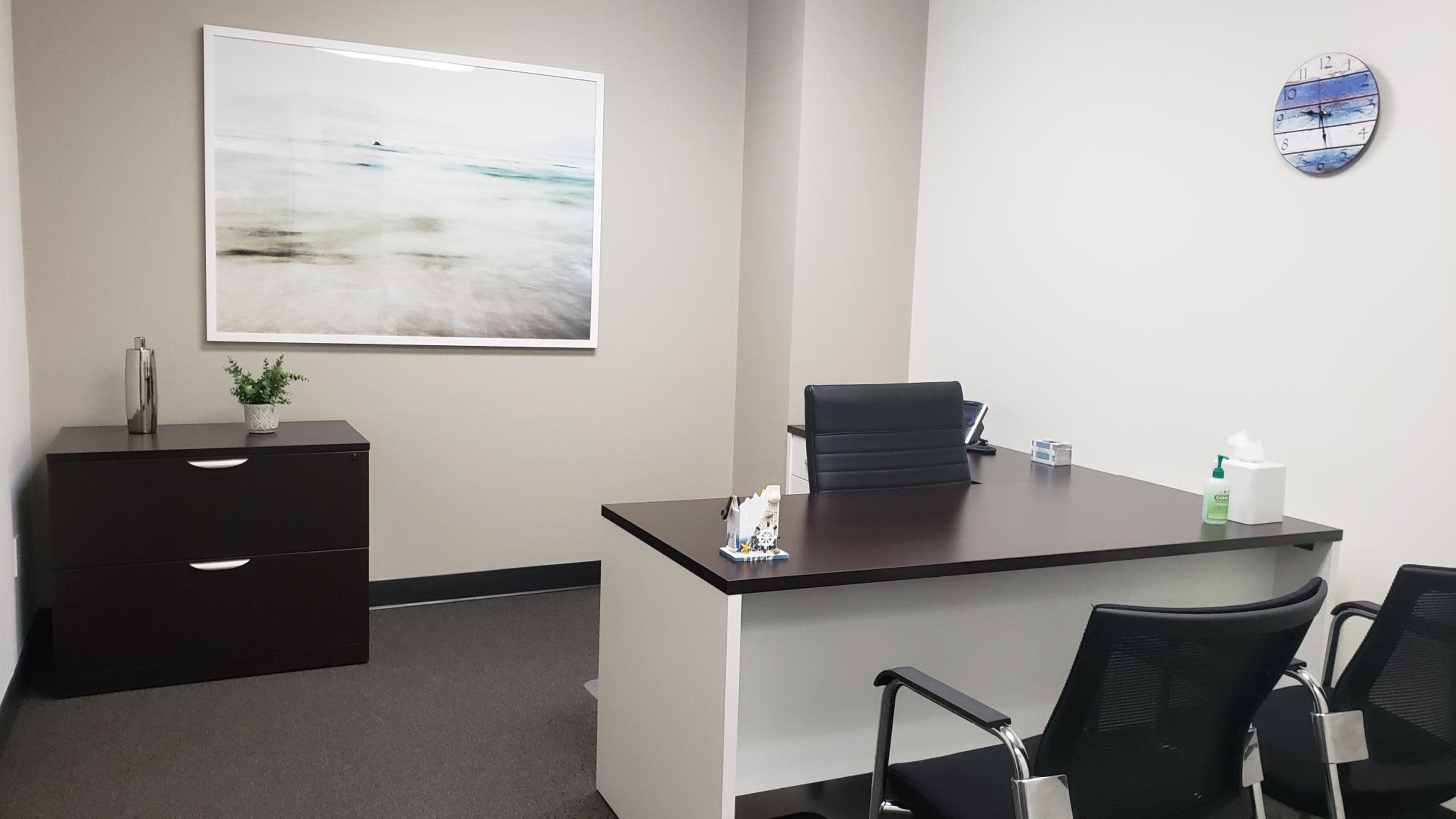A modern office space features a desk with a chair, a storage cabinet, and a wall-mounted artwork.