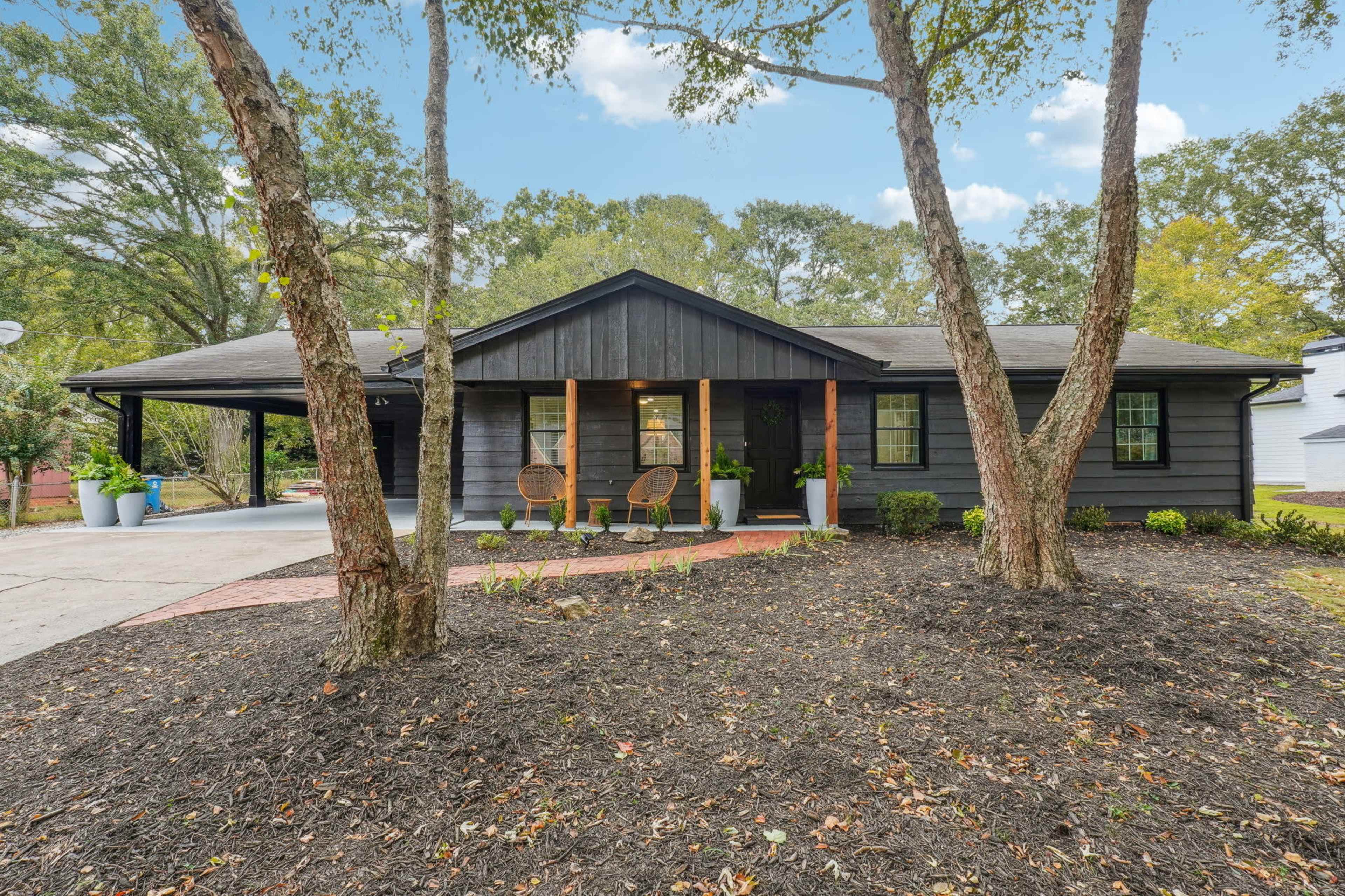 A black-painted single-story house with a covered porch, flanked by two trees and a landscaped front yard.
