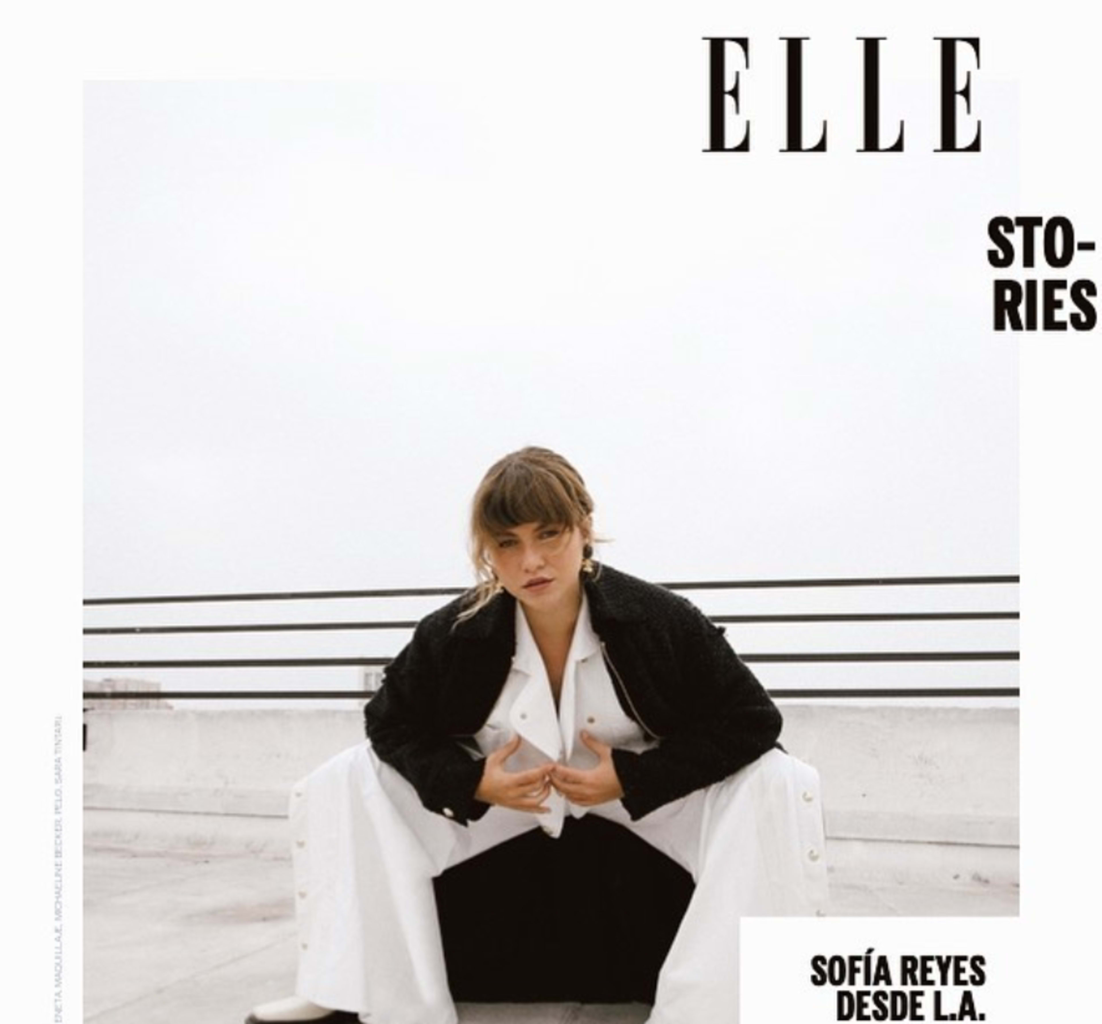 A person in a black and white outfit poses against a minimalist rooftop background.