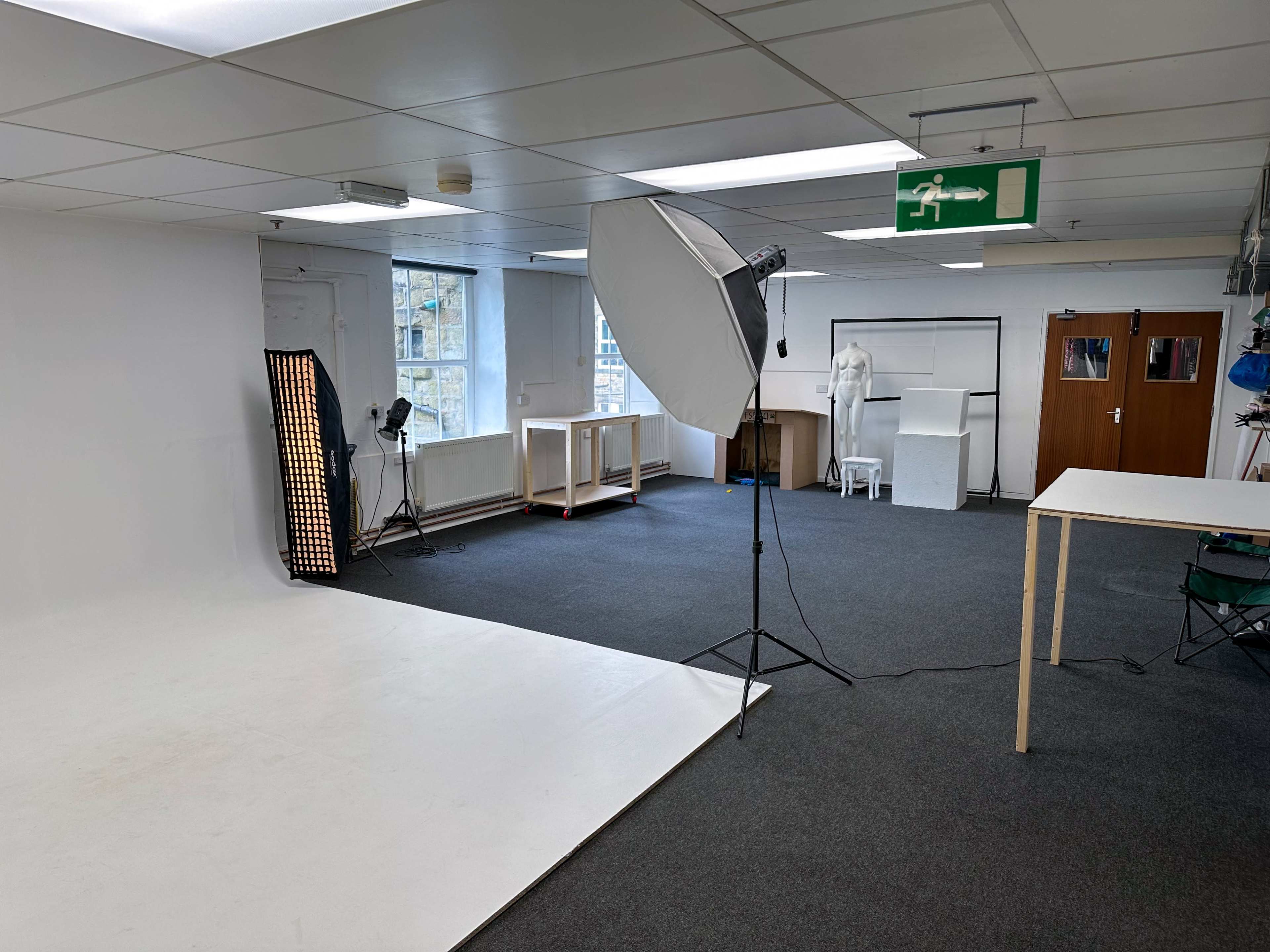 A well-lit photography studio with a white backdrop, various lighting equipment, and display tables.