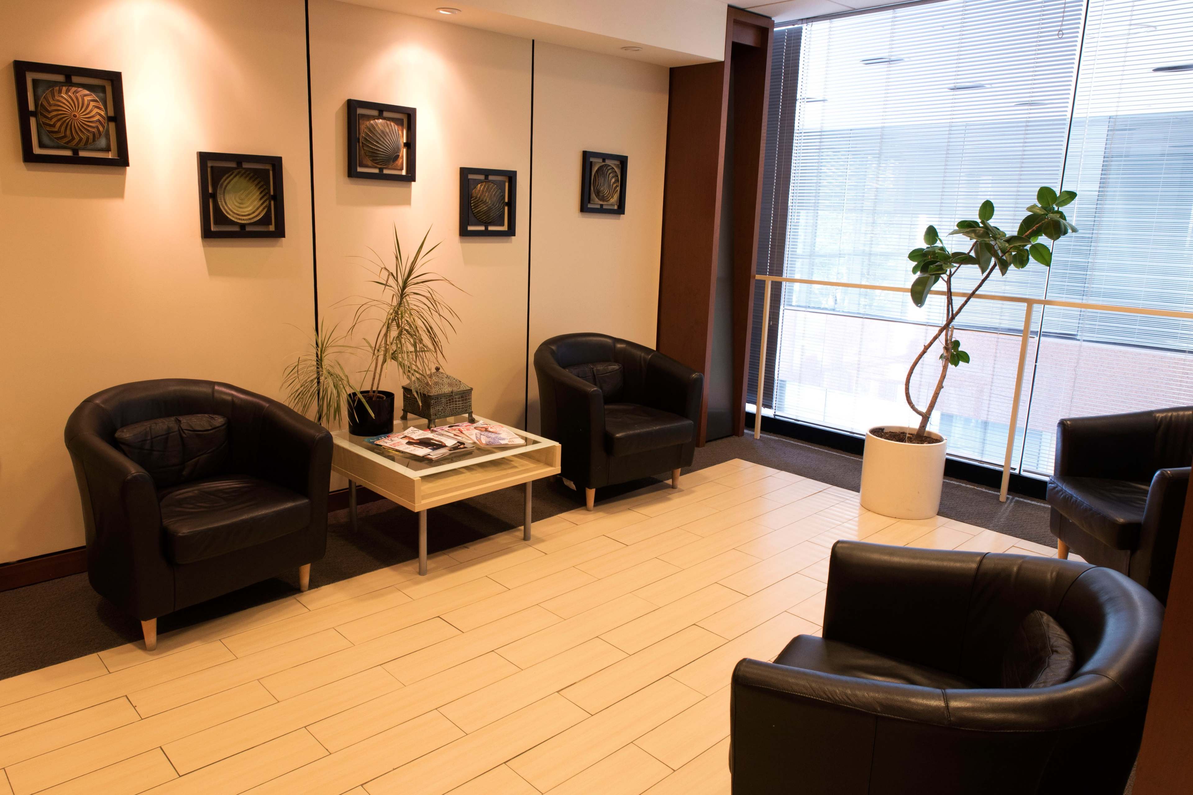 A waiting area with four black leather chairs arranged around a small table, a potted plant, and framed art on the walls.