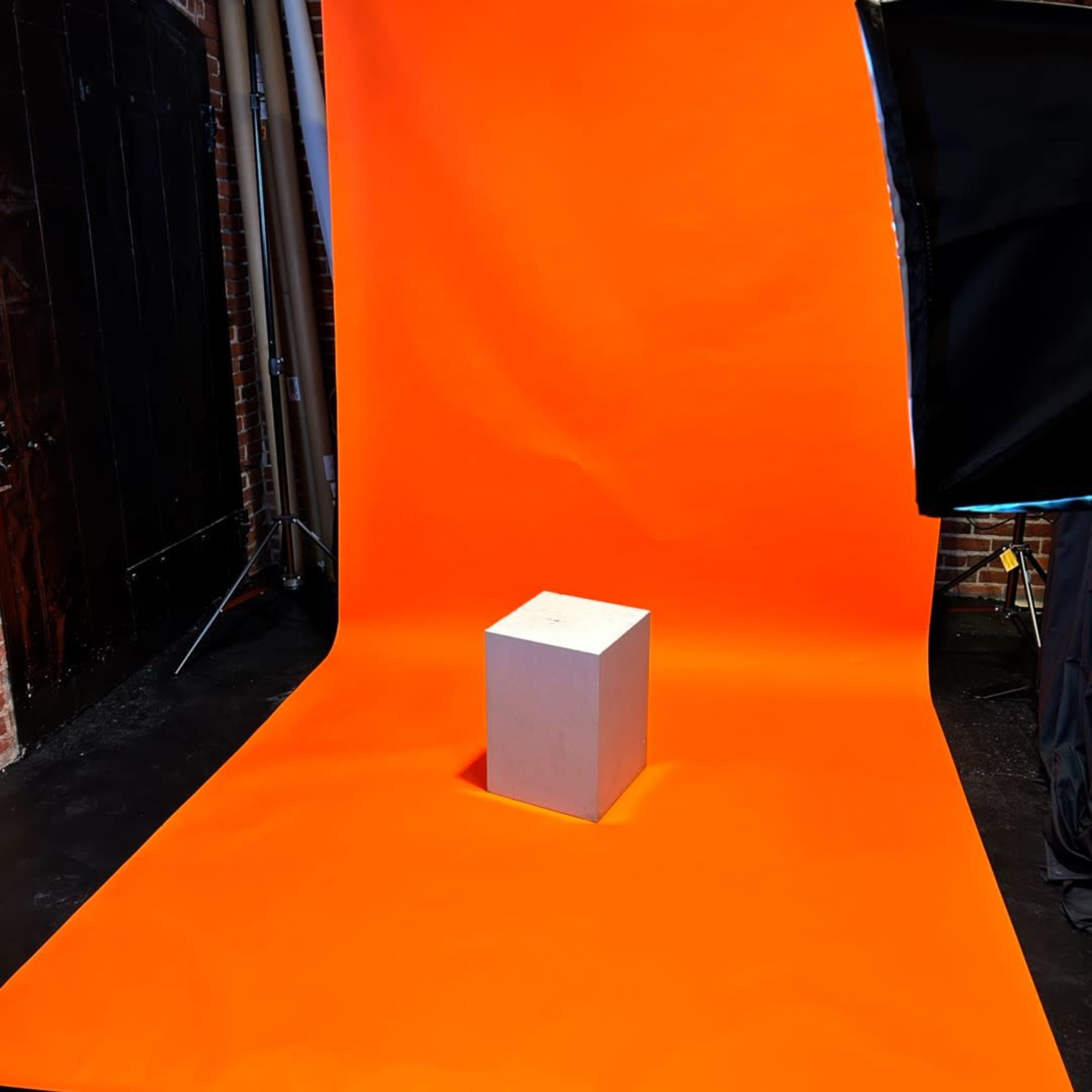 A gray cube placed on an orange backdrop in a studio setting.