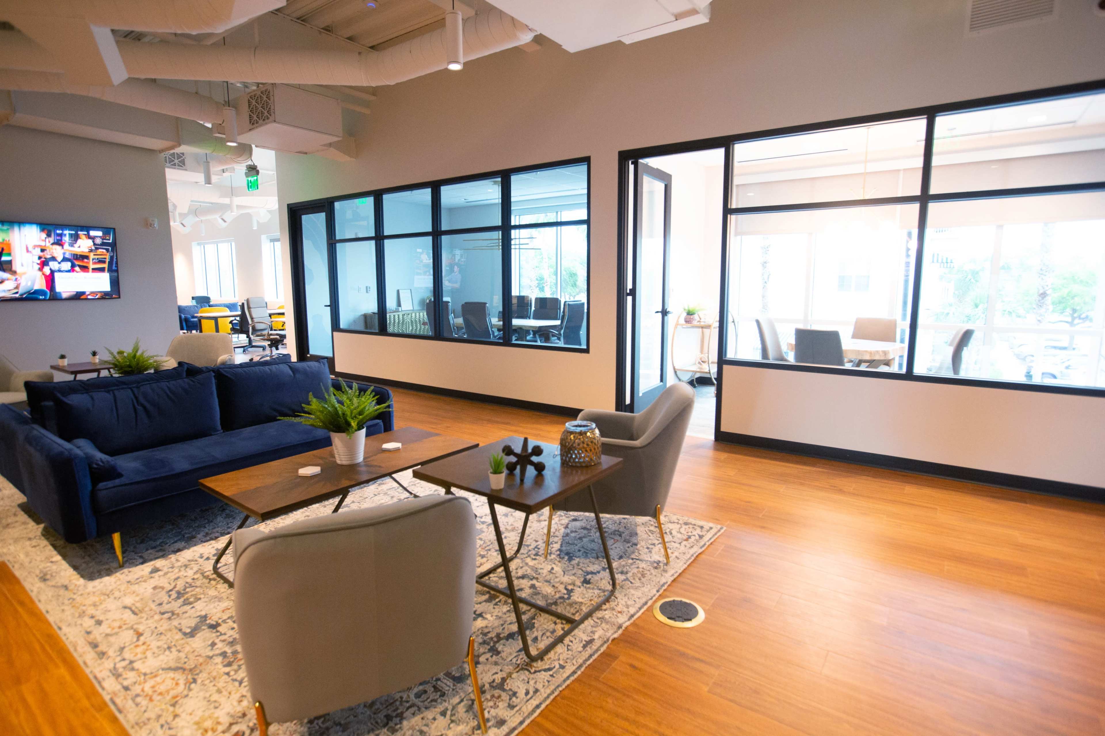 A modern office space featuring a sitting area with a navy sofa, a coffee table, and a view of glass-walled meeting rooms.