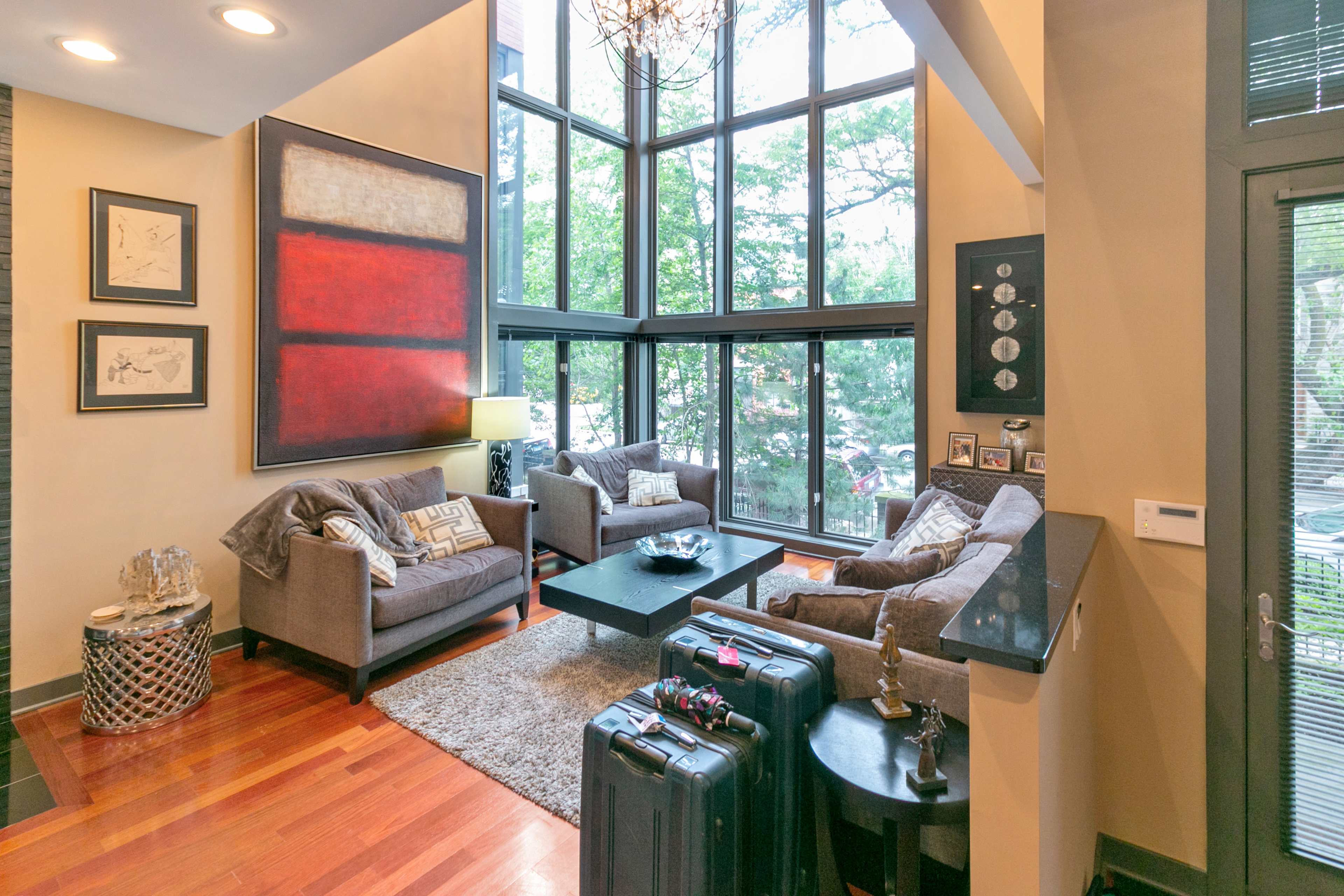 The living area features two grey sofas facing a coffee table, surrounded by large windows that provide a view of the outdoors.