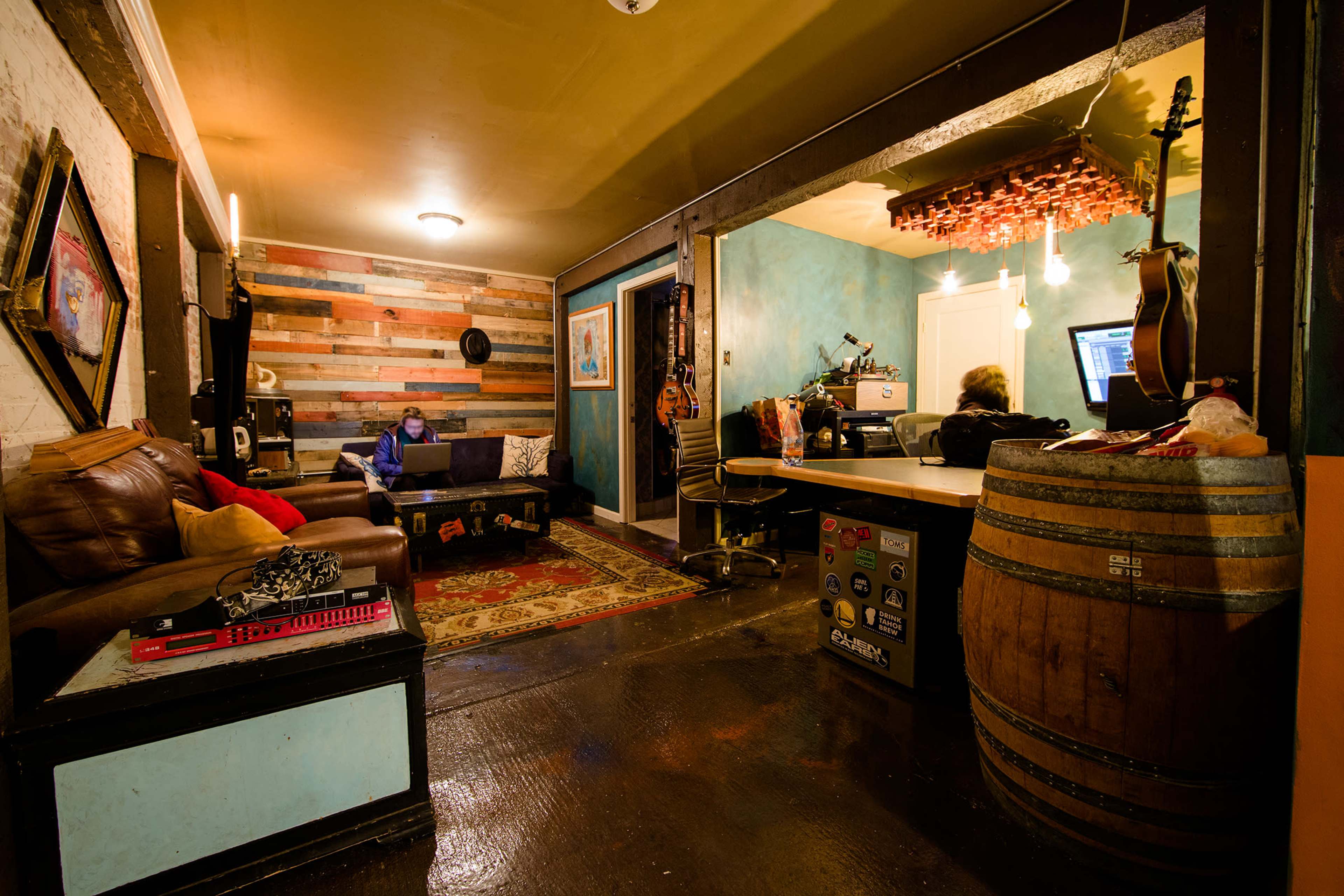 A cozy room with wooden accent walls, a leather couch, and two people working at a desk with a barrel-style table nearby.