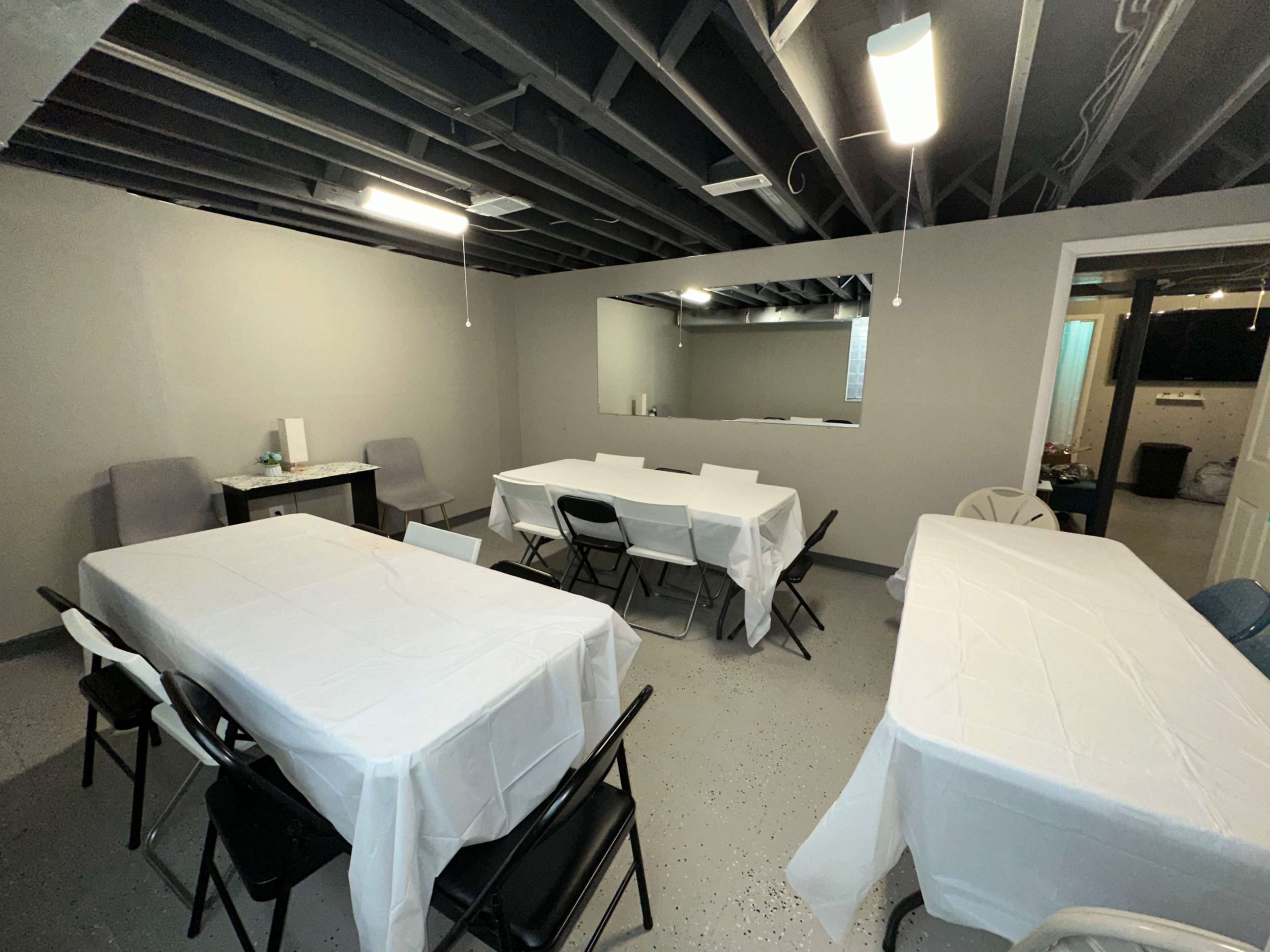 A basement meeting room features several tables covered with white tablecloths and minimalist seating arrangements.