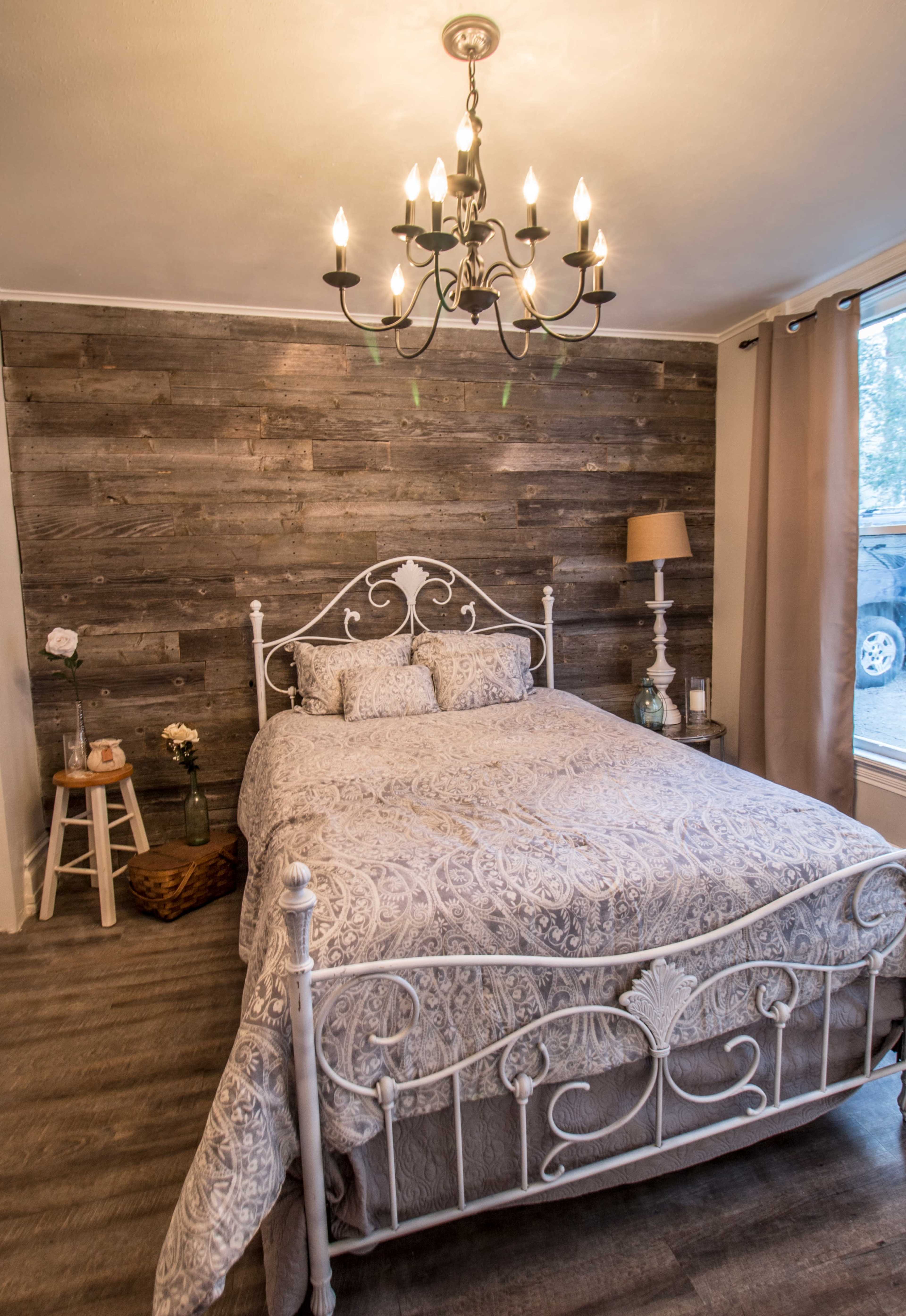 A bedroom featuring a white metal bed with a decorative quilt, a chandelier overhead, and a wooden accent wall.
