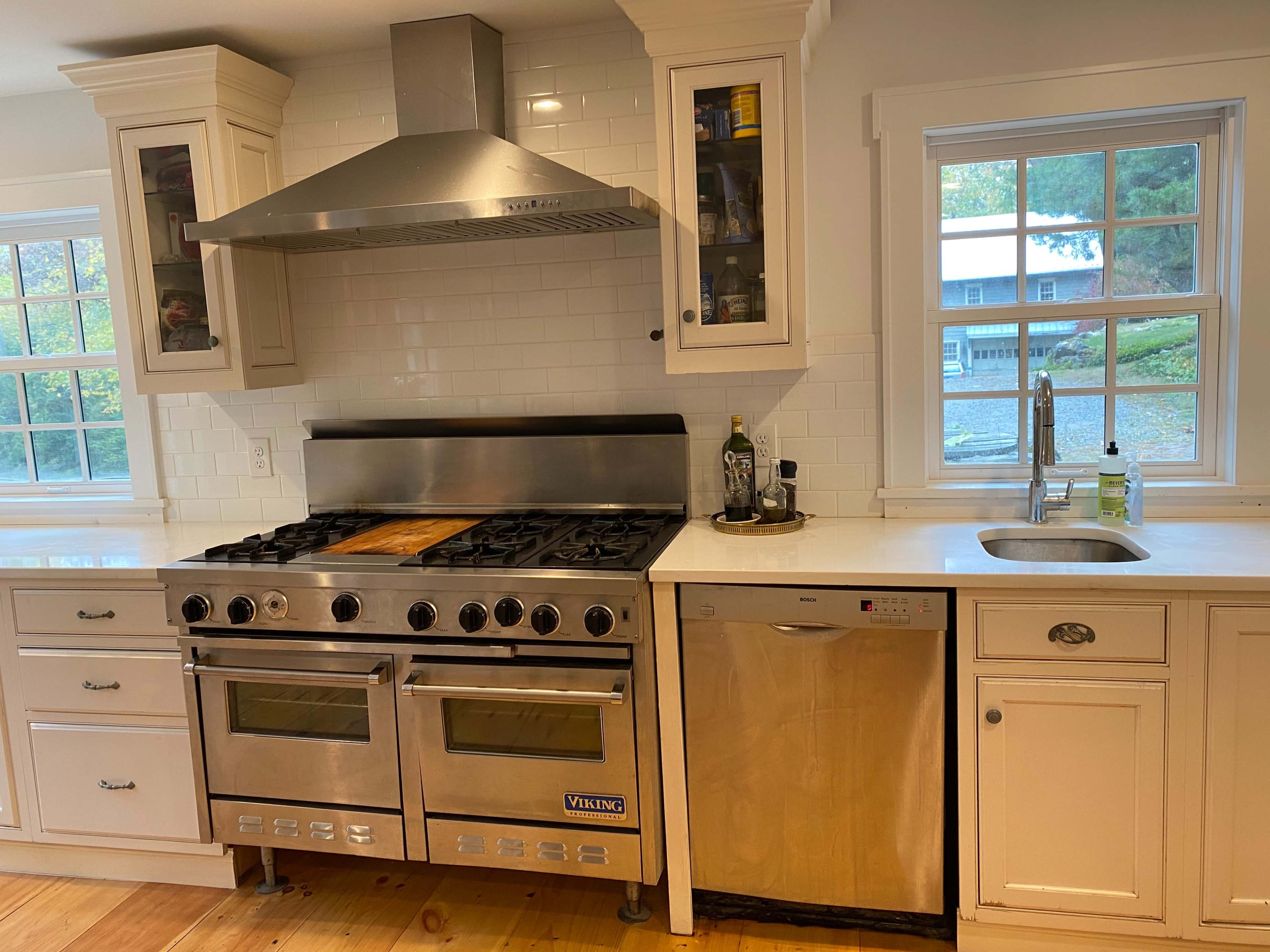 A kitchen featuring a stainless steel Viking range, a dishwasher, and a sink under a window, with white cabinetry and wood flooring.