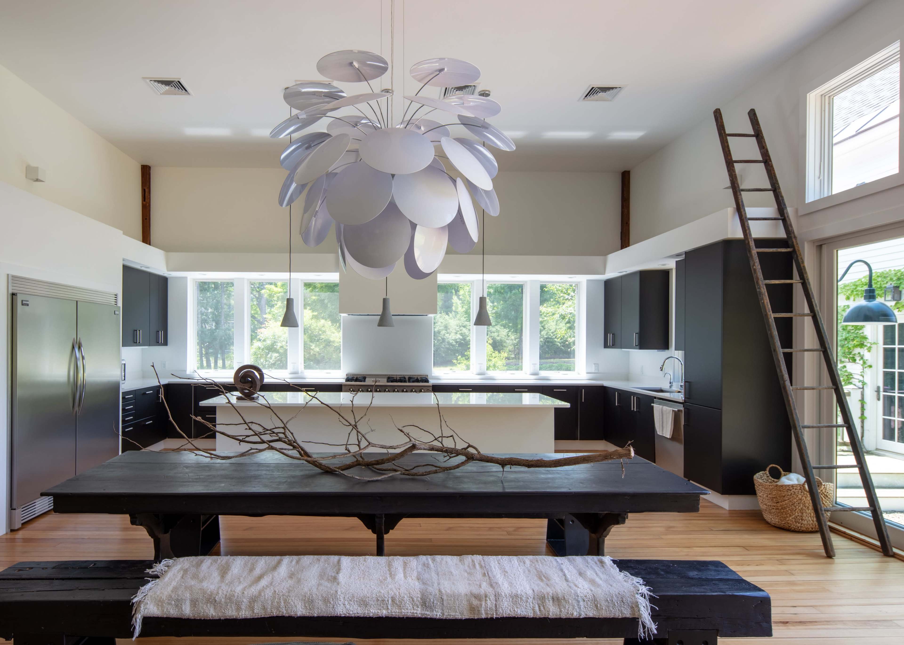 A modern kitchen featuring a large wooden dining table, a unique pendant light, and a ladder against the wall.