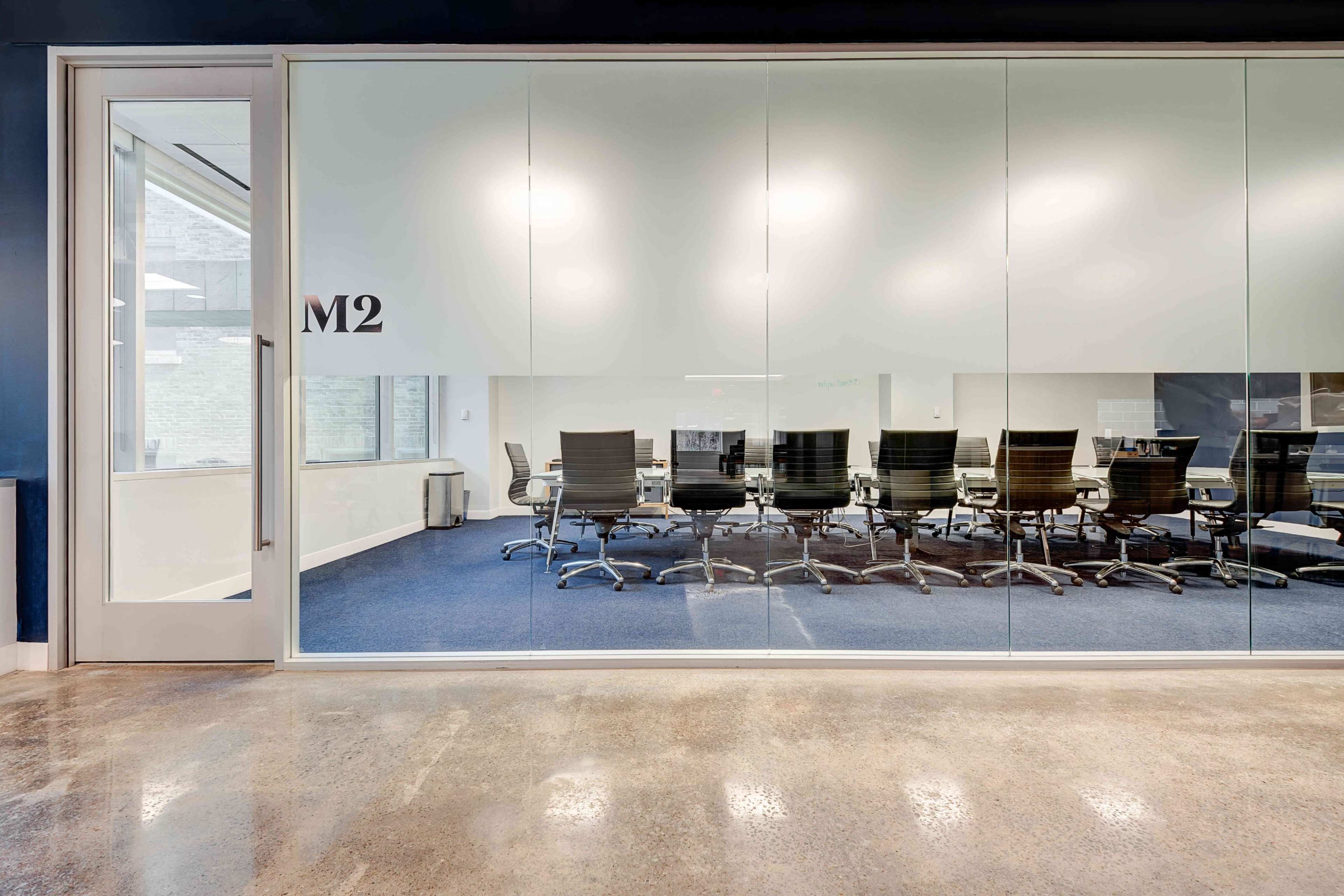 A glass-walled conference room with a rectangular table and several black chairs is visible through the door labeled "M2."