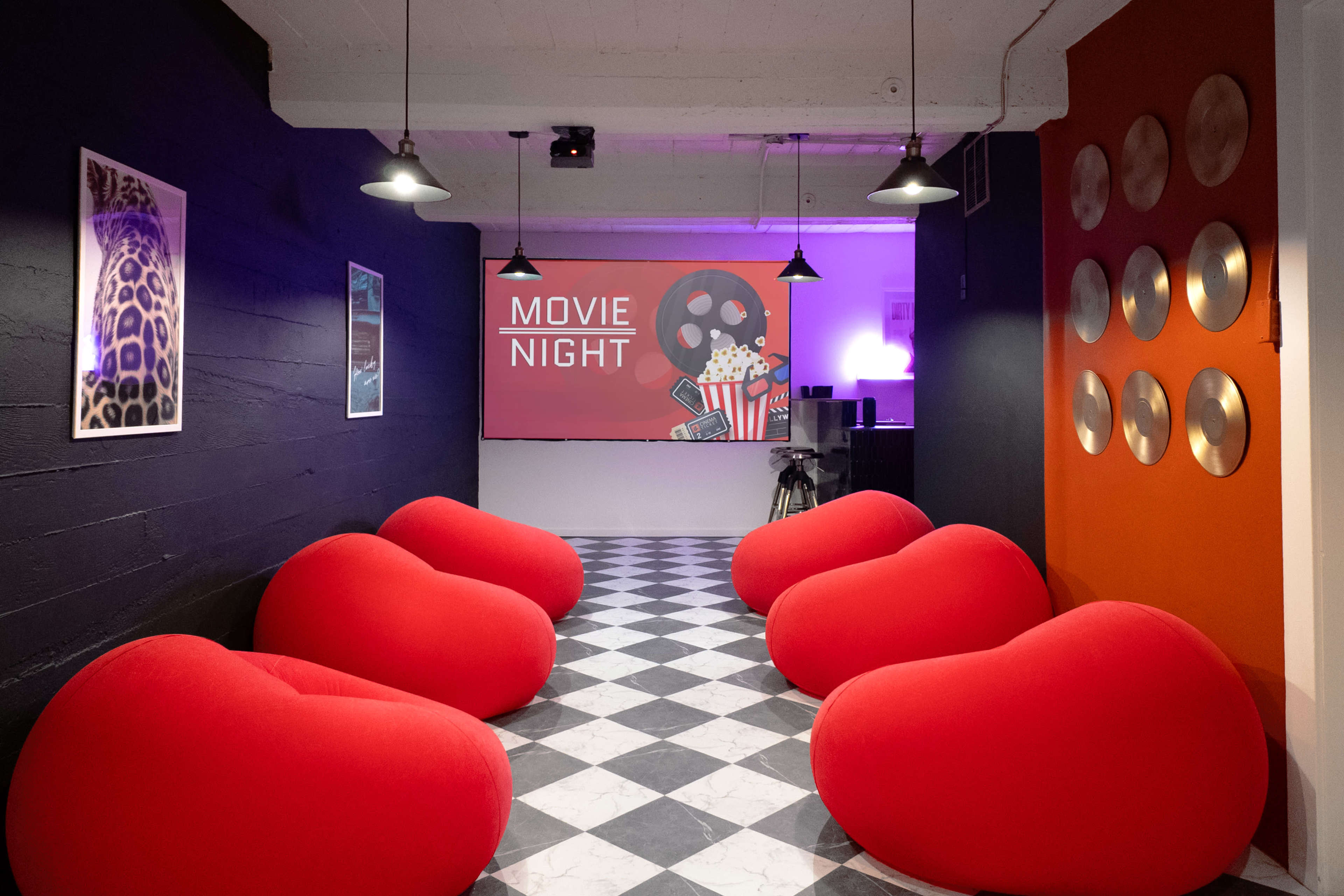 The scene features a room with large red bean bag chairs arranged in front of a screen displaying "MOVIE NIGHT," surrounded by a black and white checkered floor and various wall decorations.