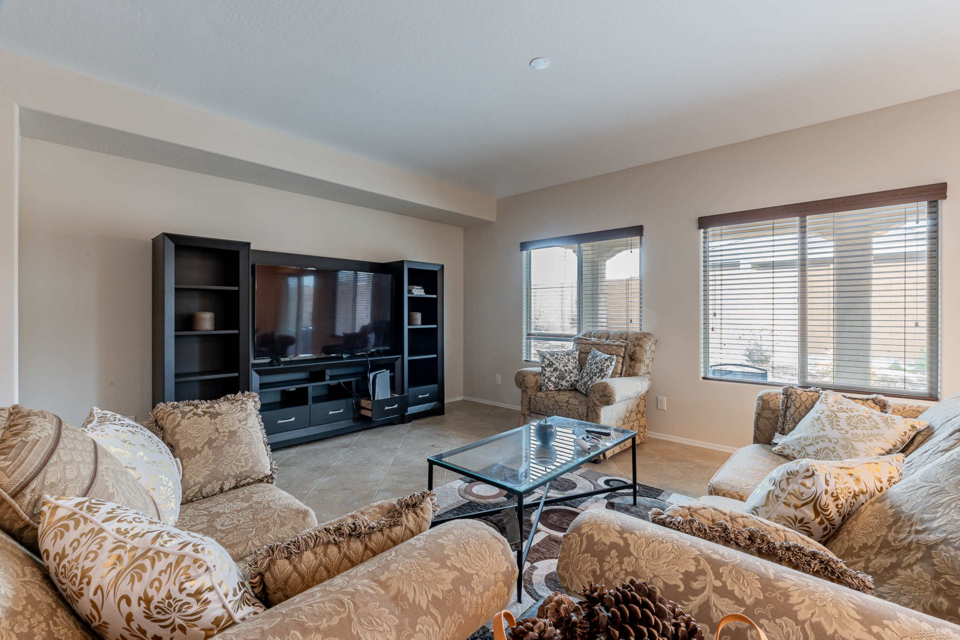 The living room features a large television unit, a glass coffee table, and upholstered seating arranged around the space.