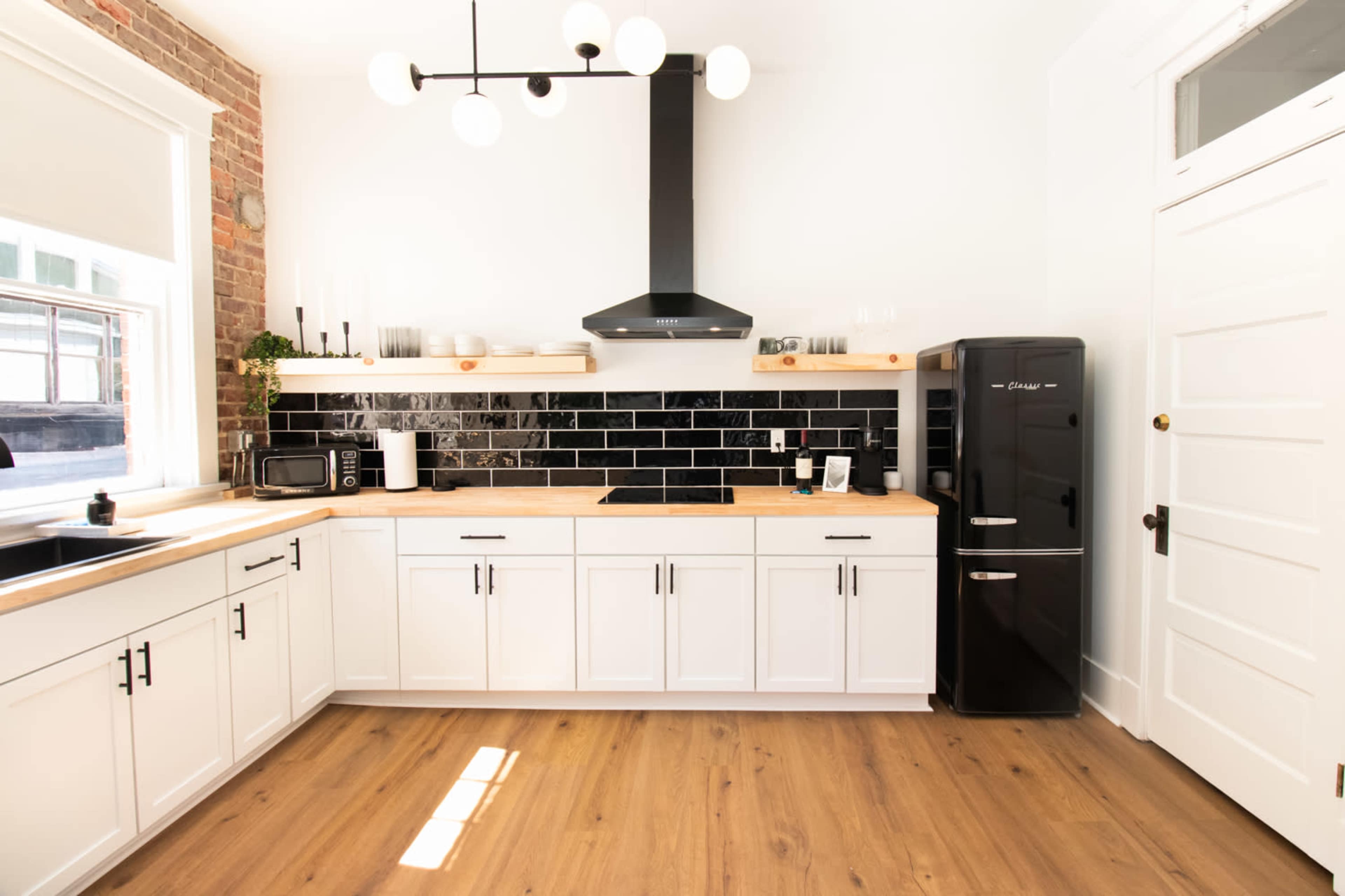 The kitchen features white cabinetry, a black backsplash, a stainless steel range hood, and wooden flooring.