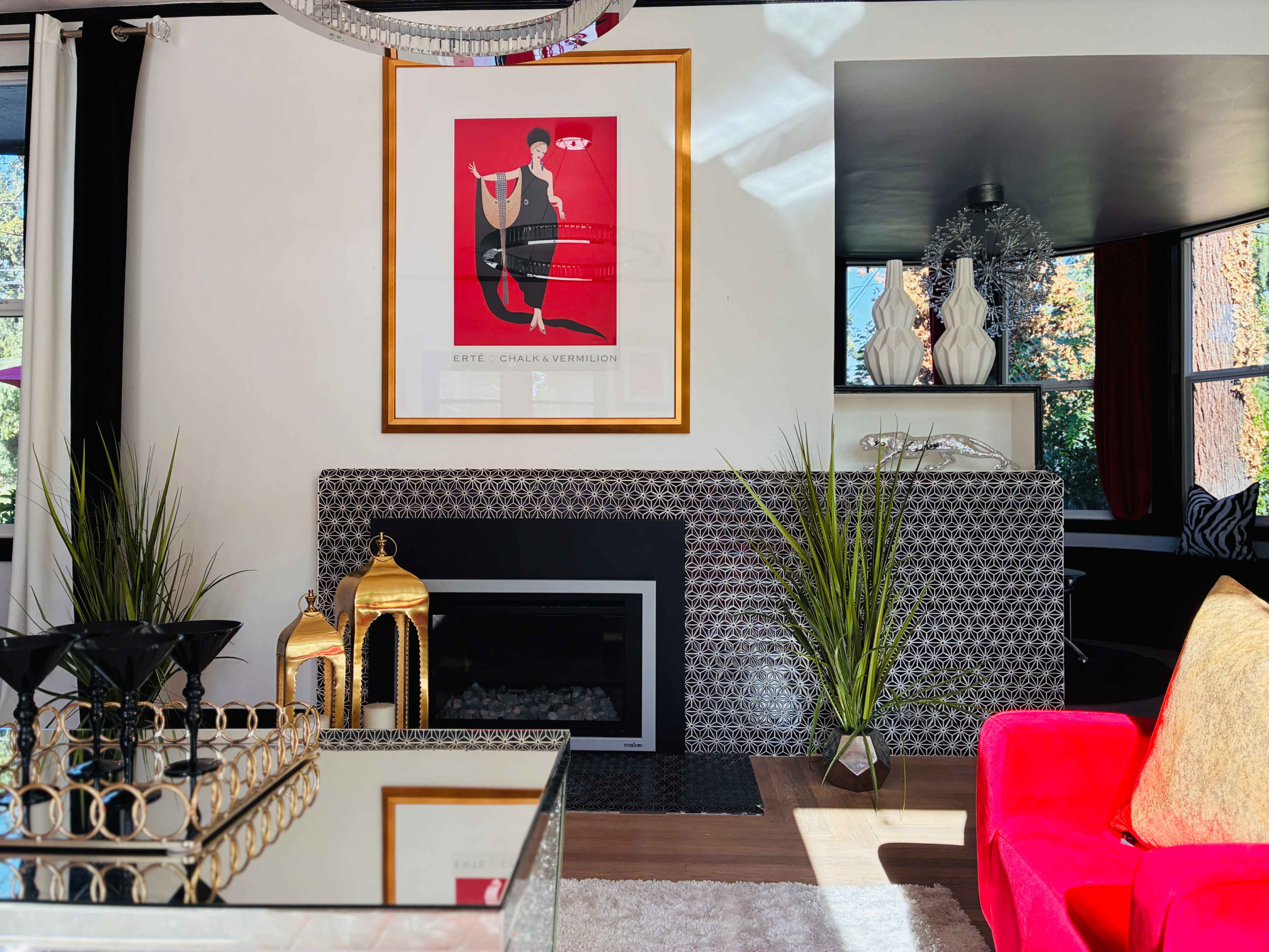 The image shows a modern living room with a stylish black and white patterned fireplace, a colorful art piece on the wall, and contemporary décor elements like a red sofa and decorative plants.