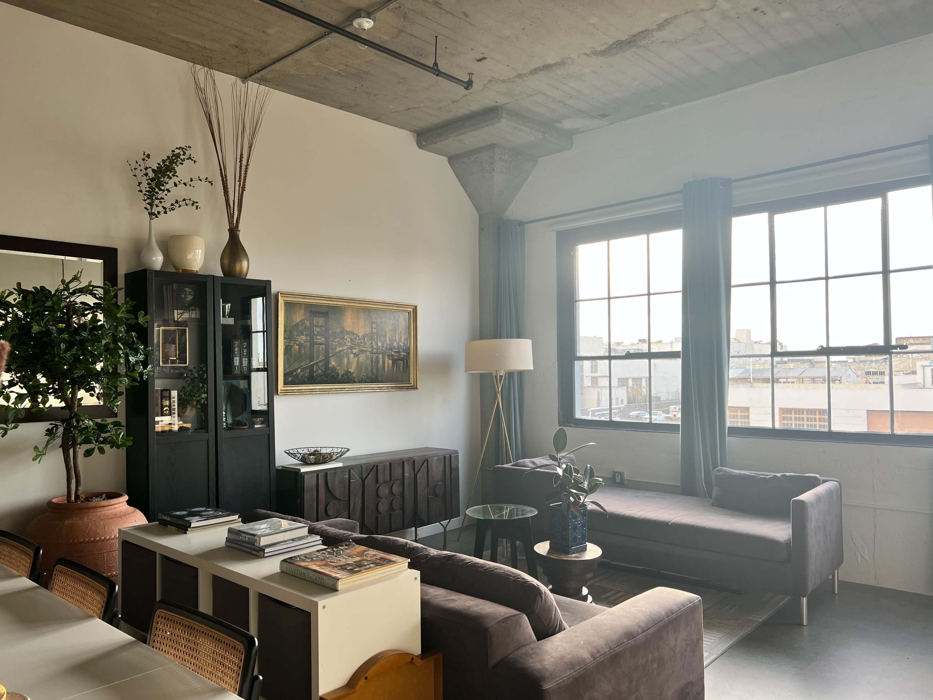 The image shows a modern living room with a large window, a dark sofa, and a coffee table surrounded by various decorative items.