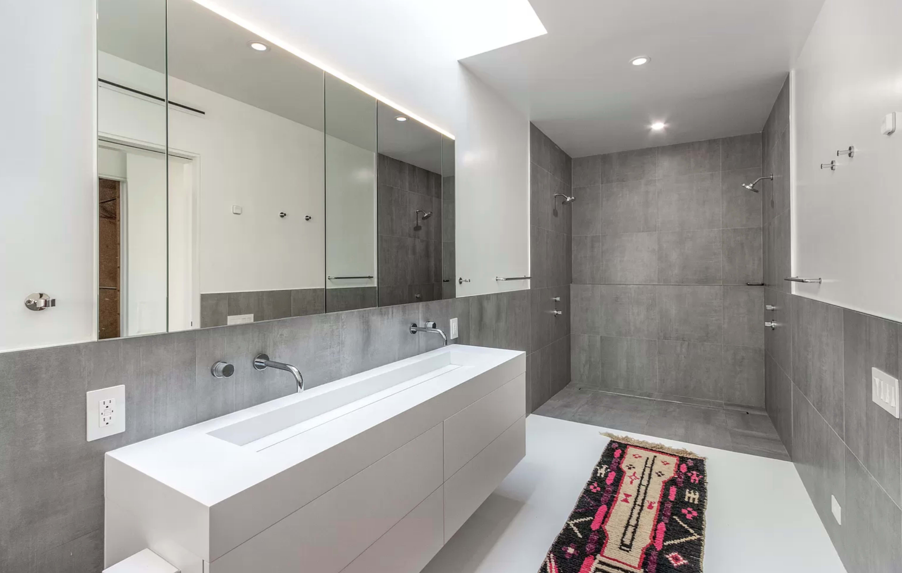A modern bathroom featuring a sleek double sink vanity, large mirrors, and a spacious walk-in shower area with gray tile walls.