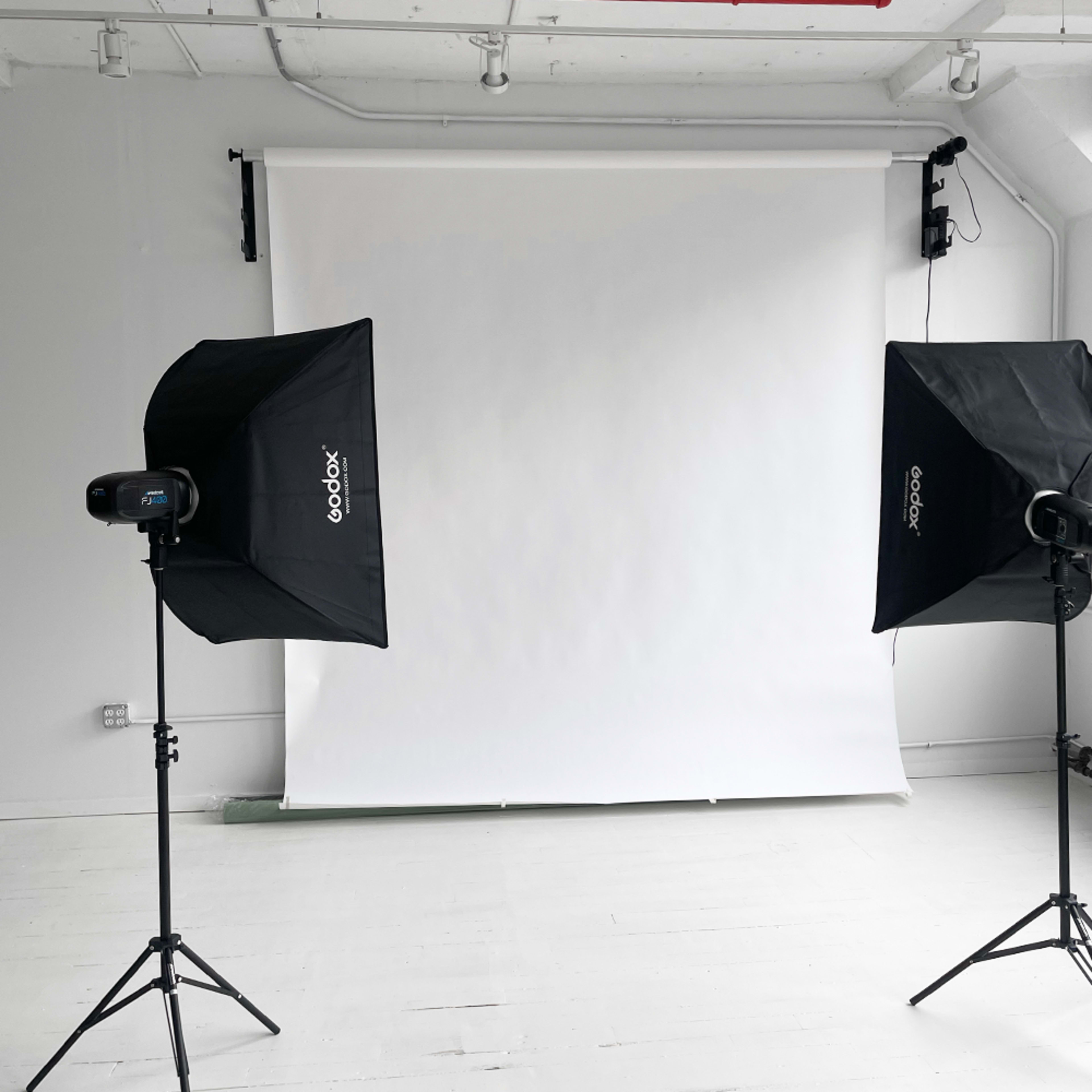 The image shows a photography studio setup with two softbox lights positioned on either side of a plain white backdrop.