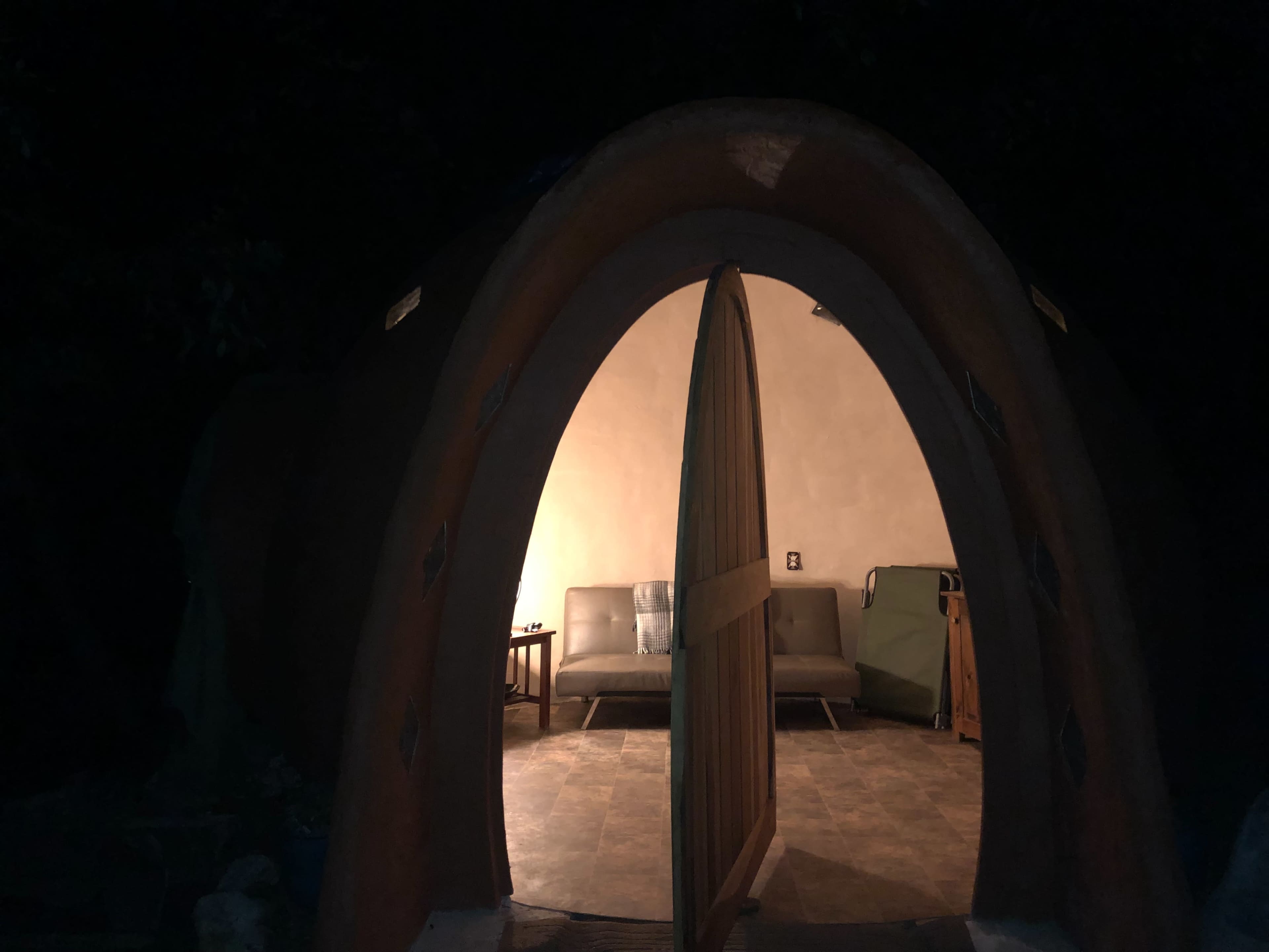 A curved entrance reveals a cozy interior with two couches and a side table, illuminated by warm light in a dimly lit environment.