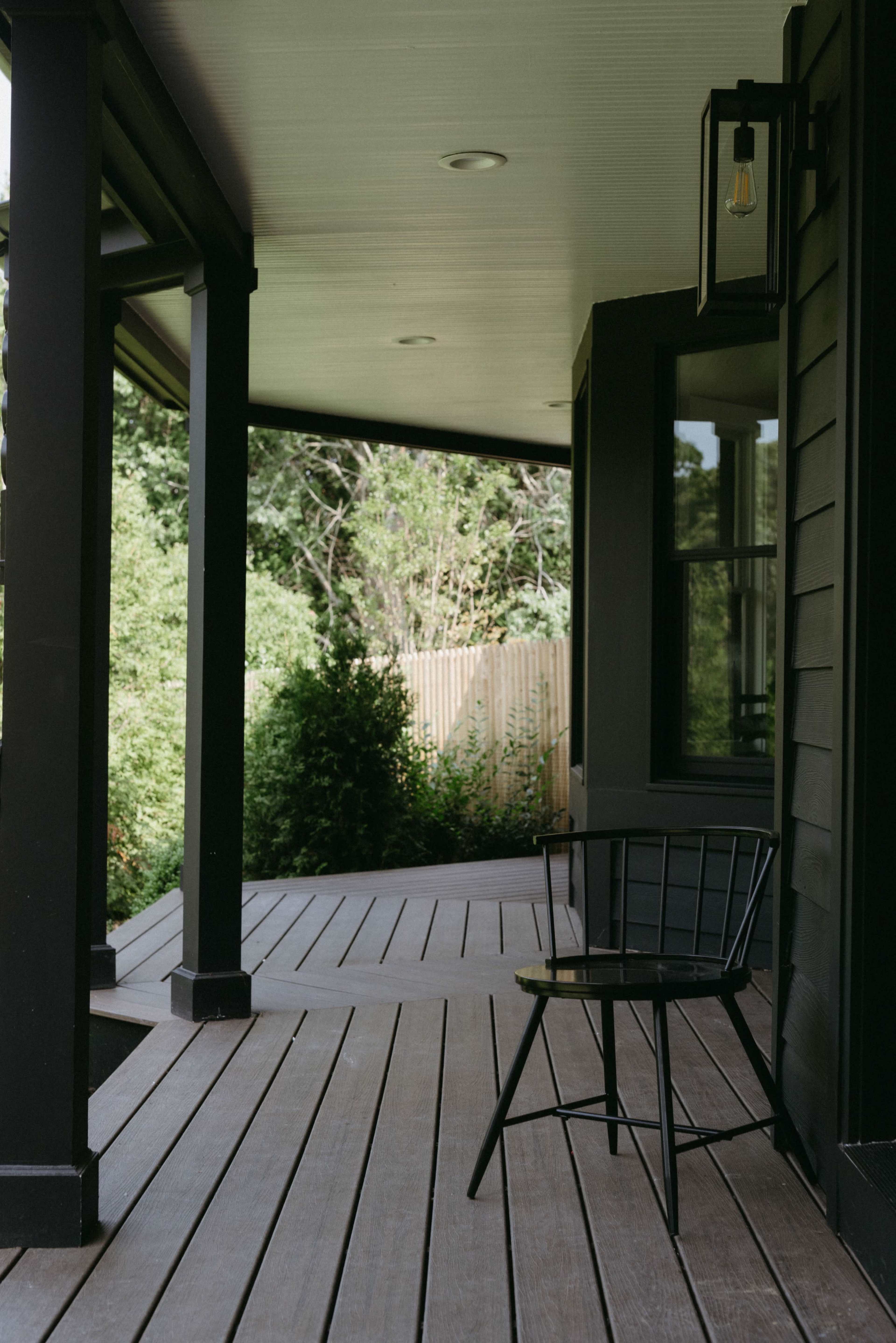 A black chair is positioned on the wooden porch, which features dark beams and a view of greenery through the railing.