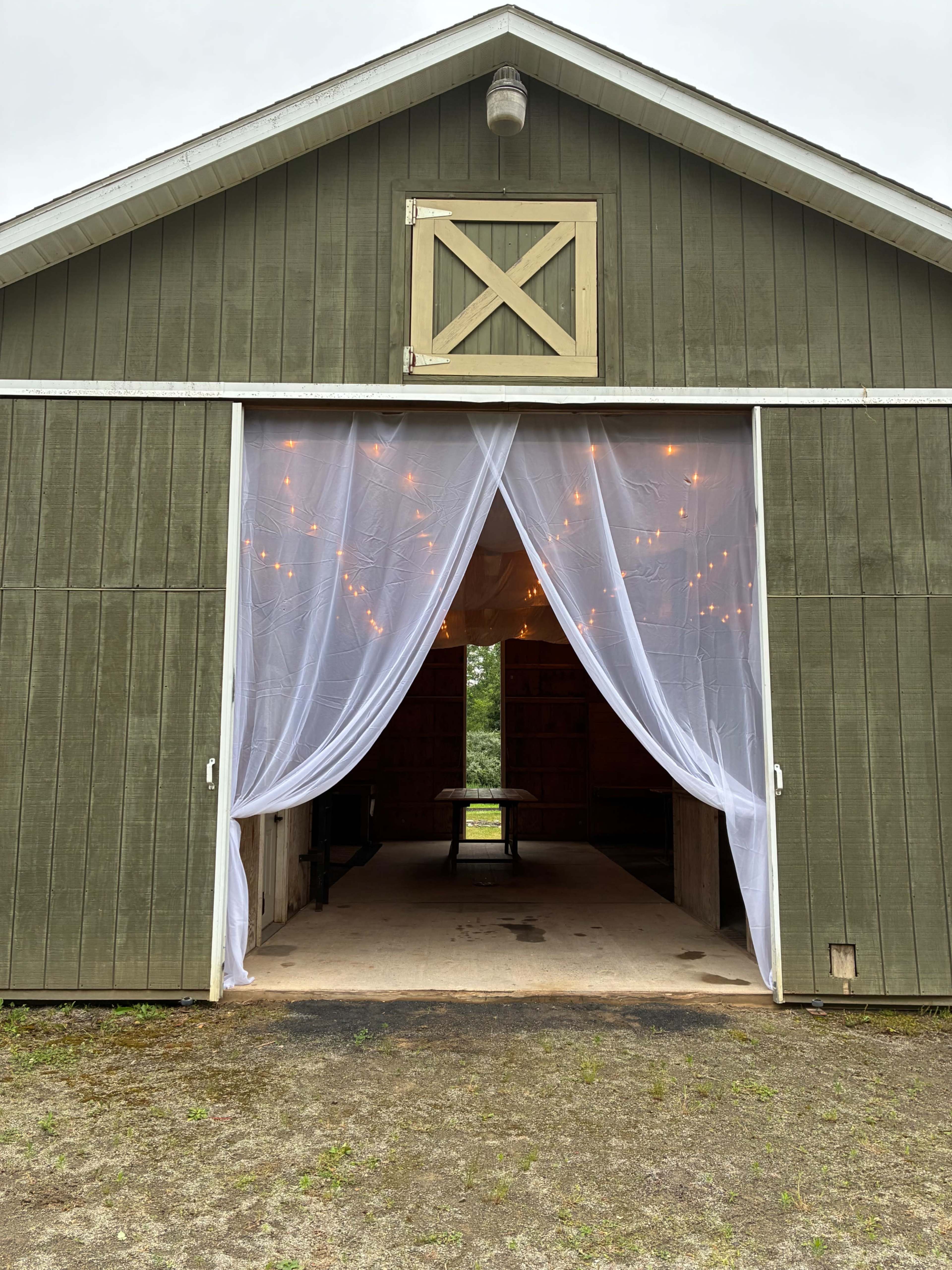 A large green barn features white sheer curtains and string lights at its entrance, revealing a glimpse of the interior.