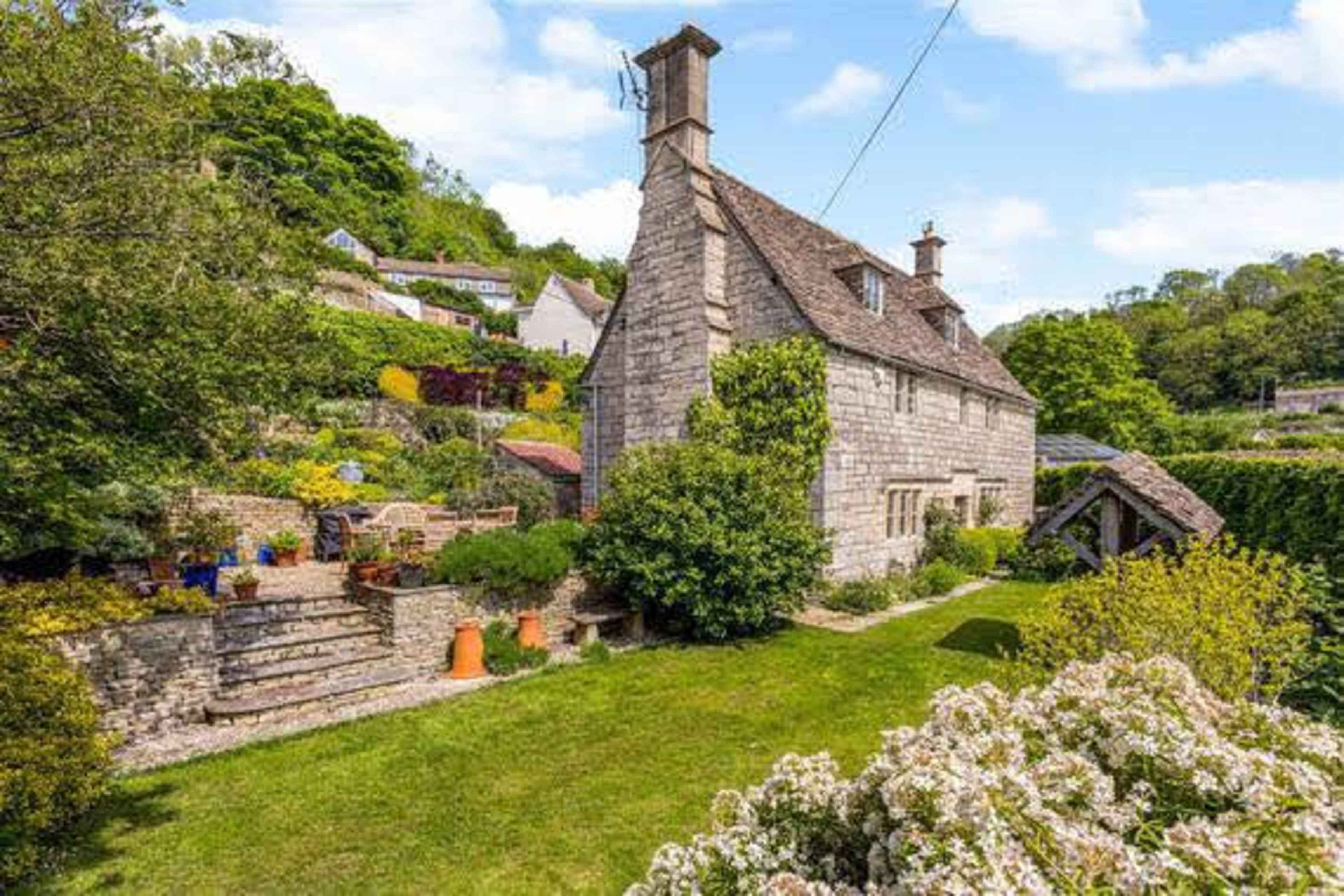 A stone cottage surrounded by a lush garden and landscaped greenery.