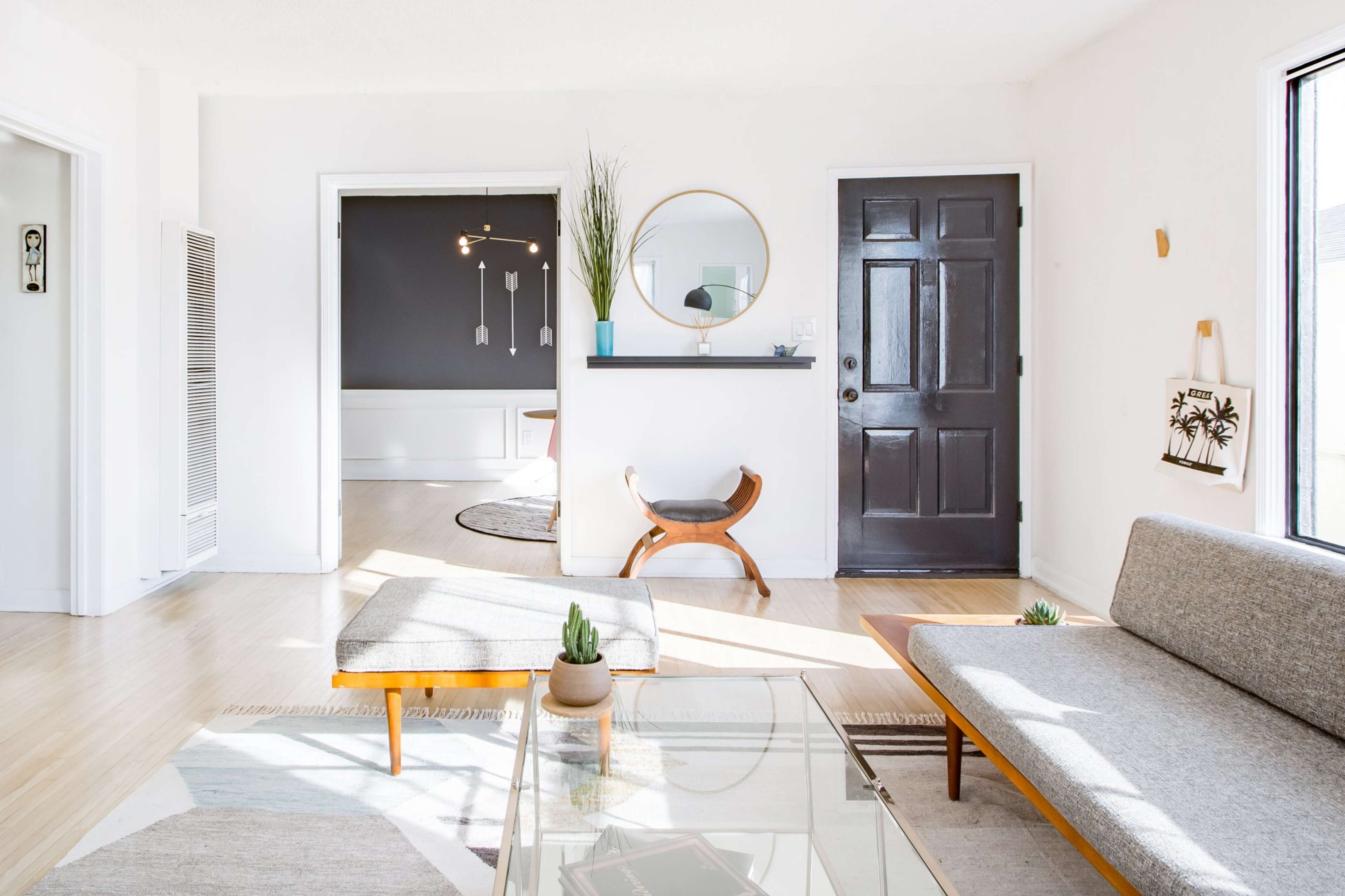 A well-lit living room with a gray sofa, a glass coffee table, and a black front door leading to a hallway.