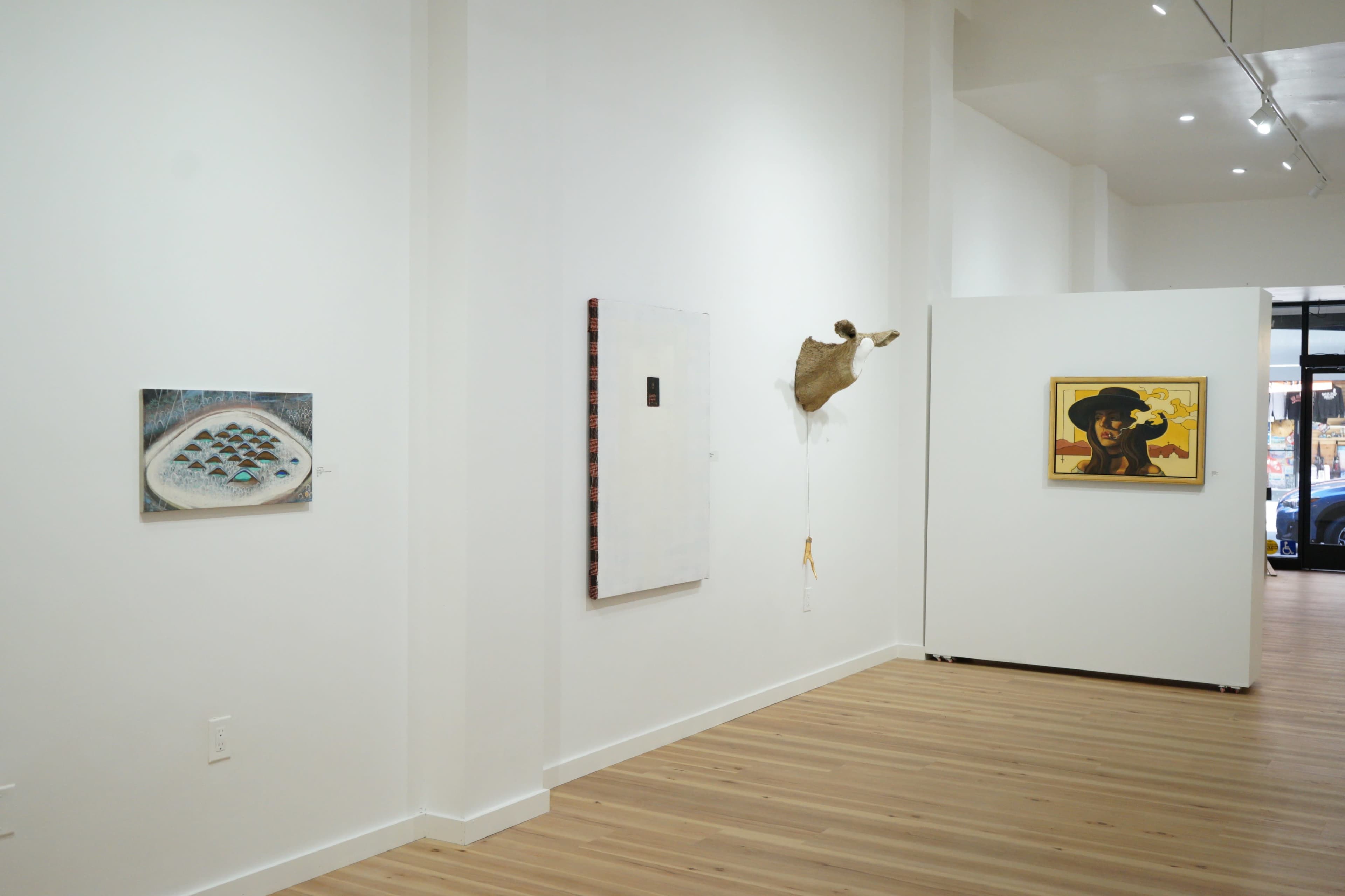 The image shows a minimalist art gallery interior featuring four artworks displayed on white walls, with a wooden floor visible.