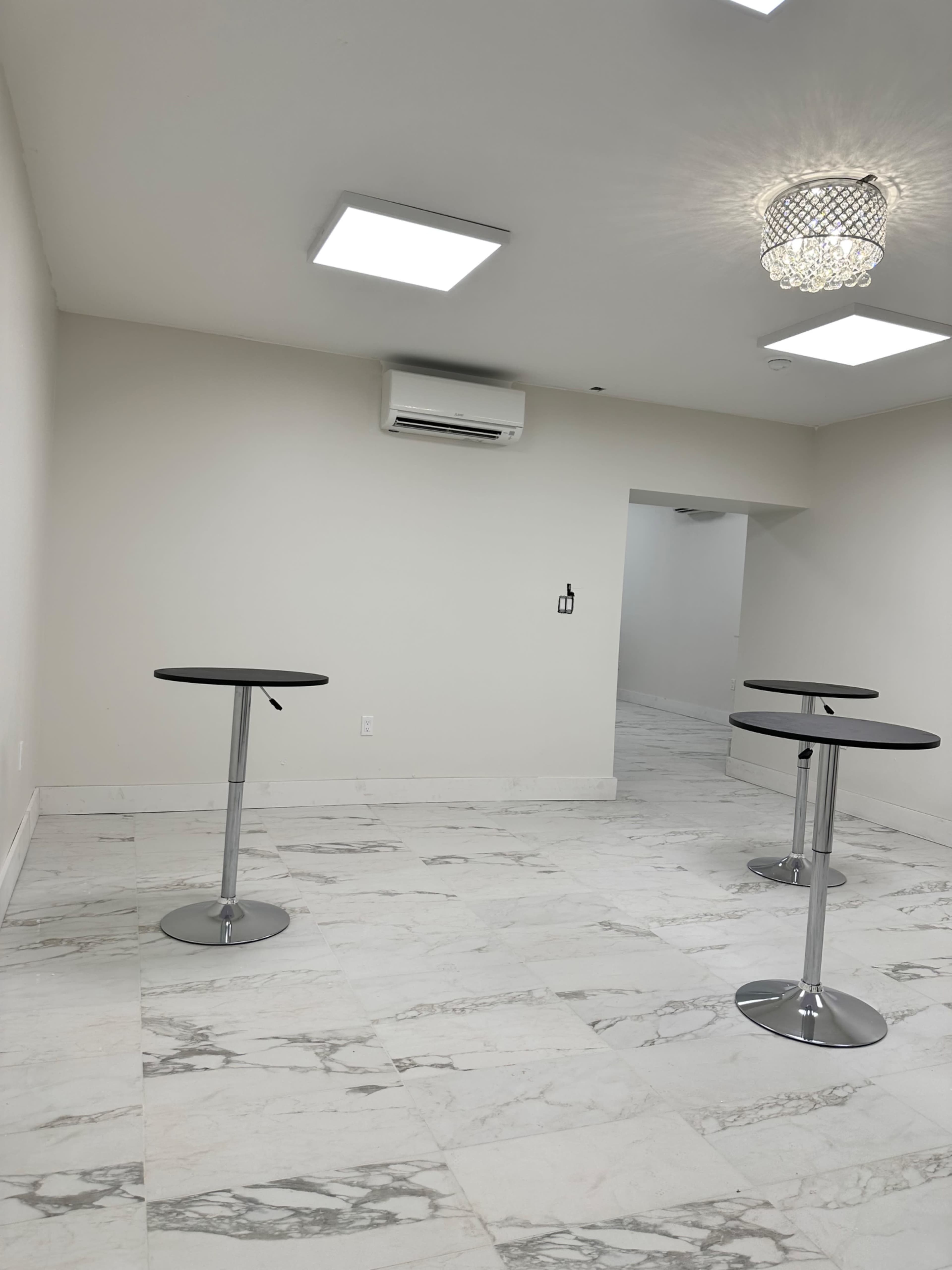 A minimalist room with white marble flooring, two high-top tables, and a stylish ceiling light fixture.