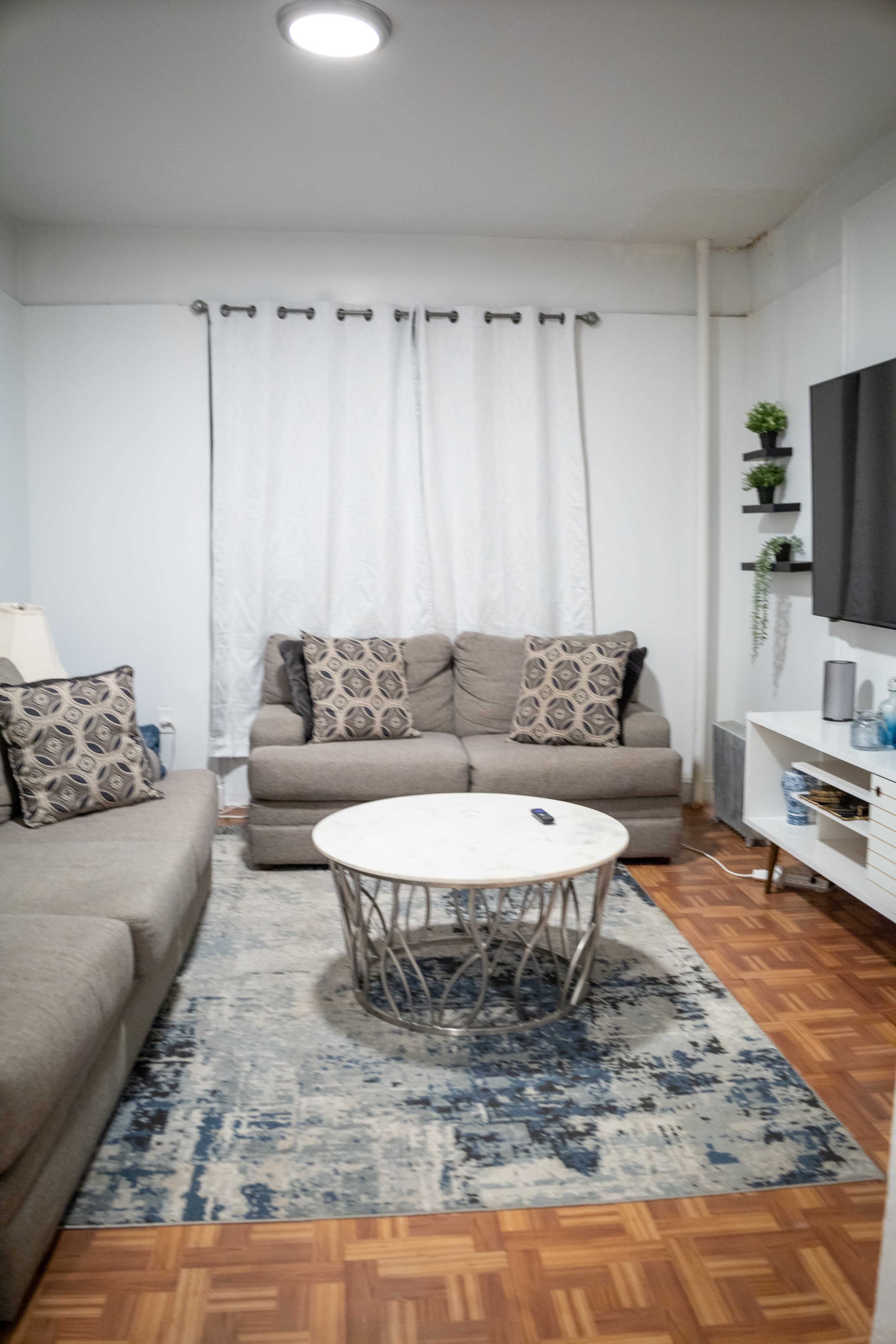 A living room with two gray sofas, a round coffee table, and a large area rug on a wooden floor.