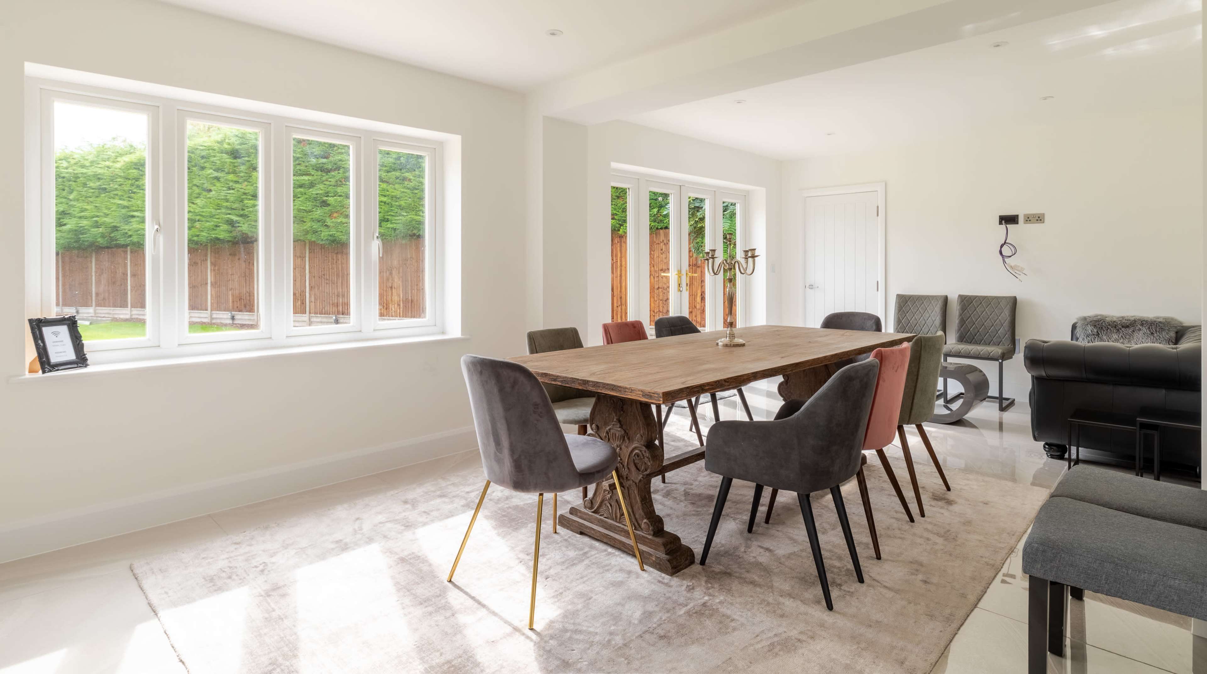 A spacious dining area features a large wooden table surrounded by upholstered chairs, with large windows allowing natural light to fill the room.