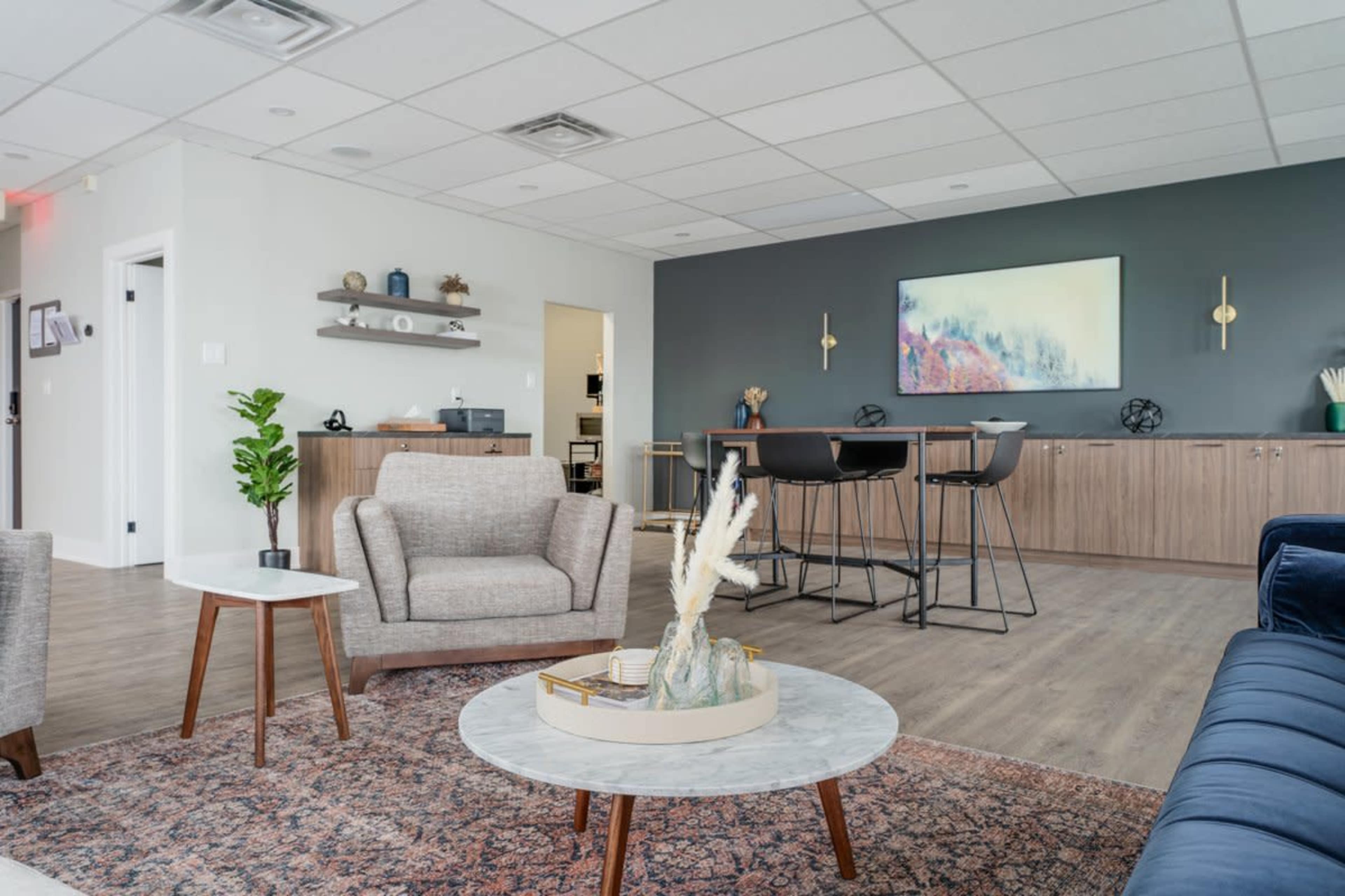 A modern lounge area with two armchairs, a round coffee table, and a bar-height dining setup against a gray accent wall.