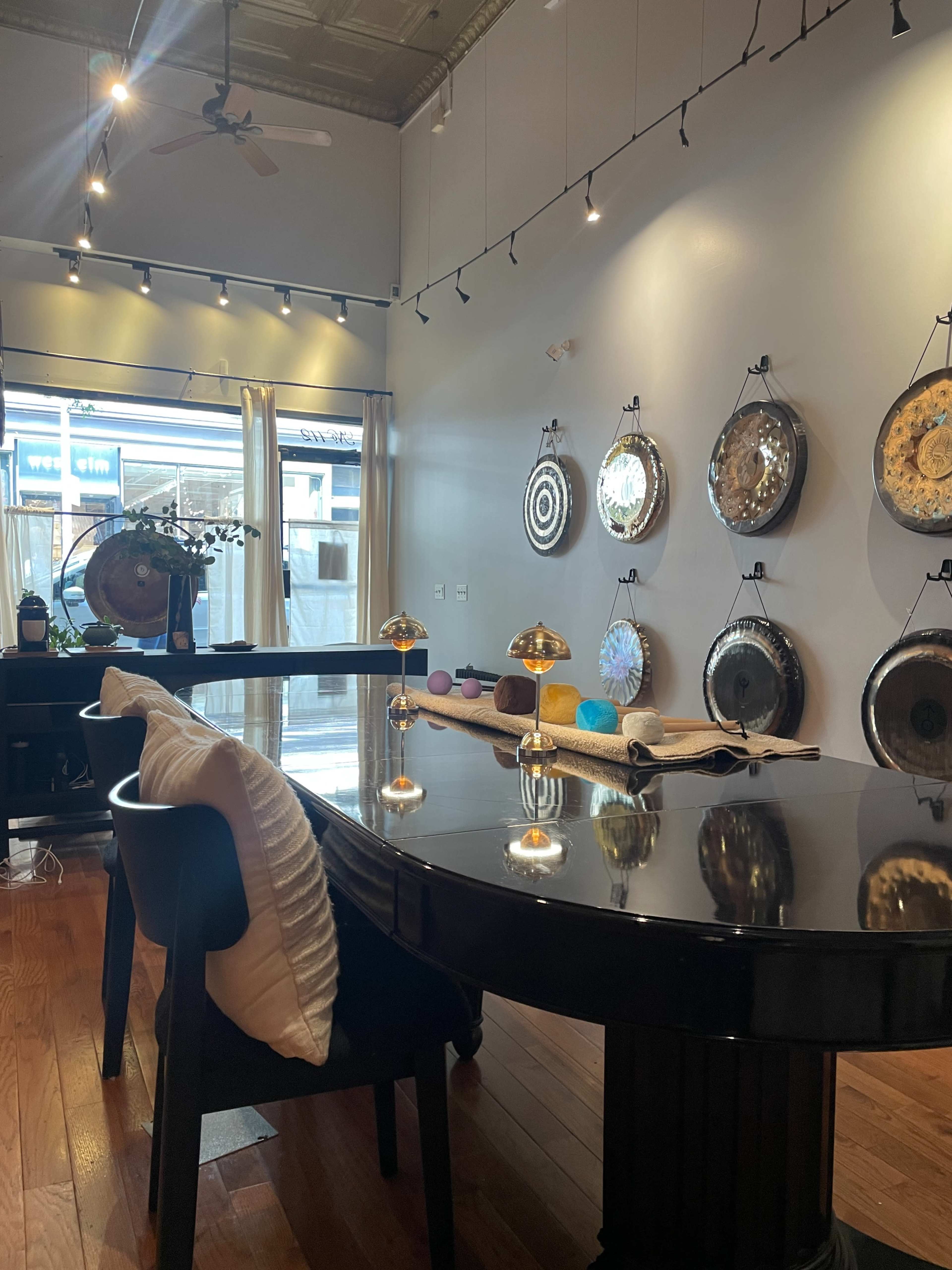 The image shows a modern interior space with a large black table, decorative wall hangings, and soft lighting.