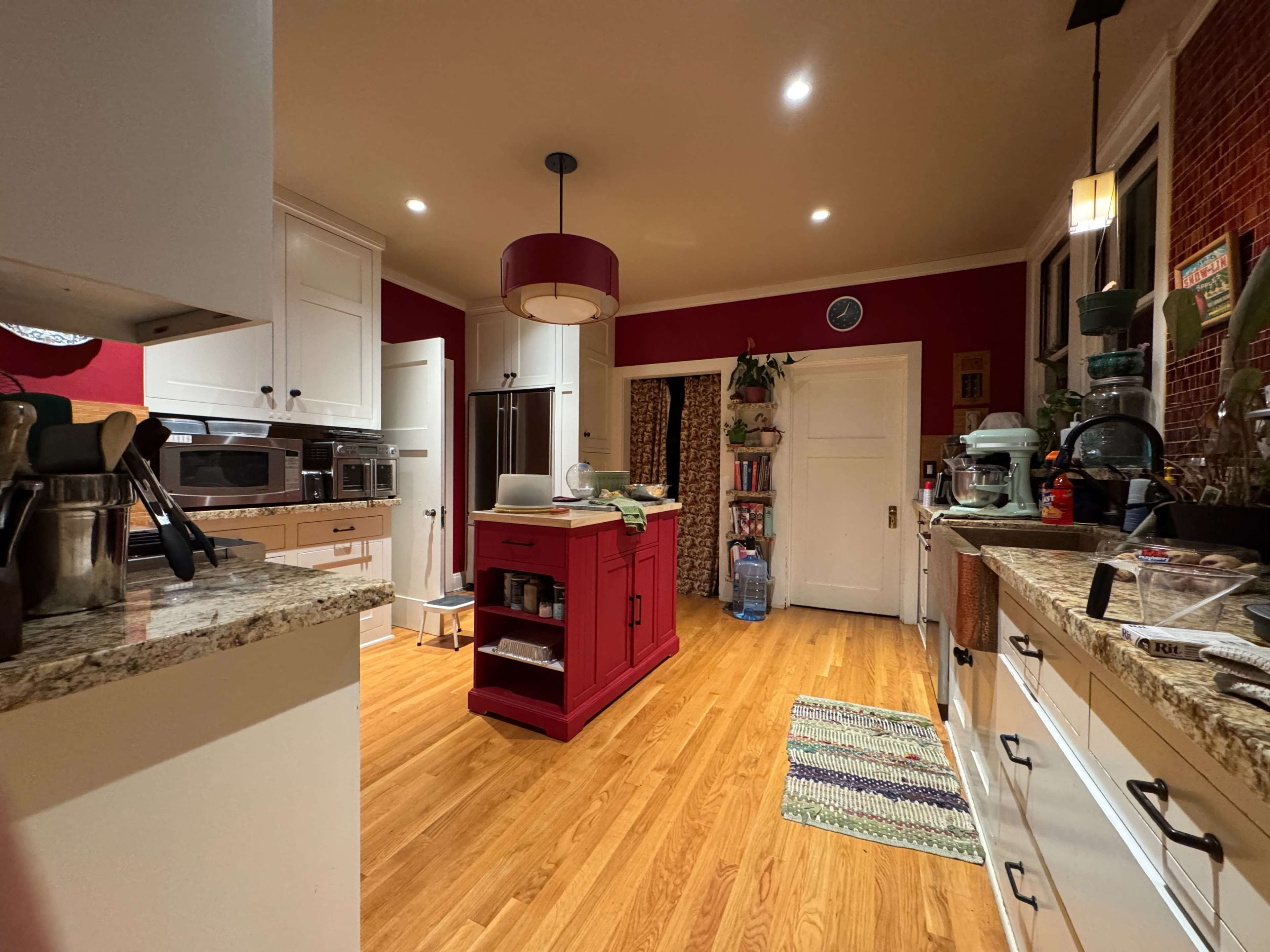 A kitchen features red accents, wooden flooring, and modern appliances arranged around a central island.