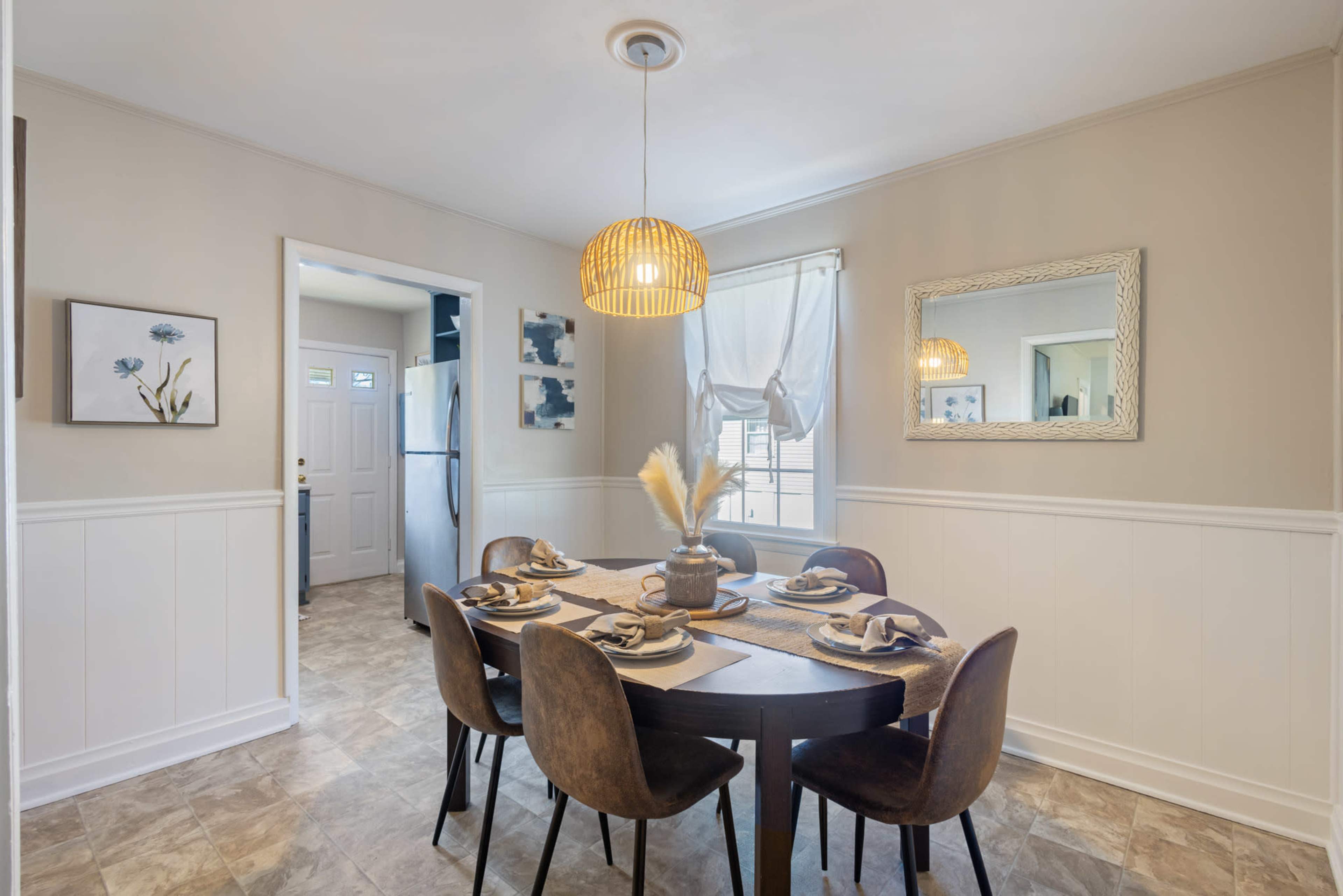 A round dining table set for four sits in a well-lit kitchen area, featuring wall decor and a pendant light overhead.