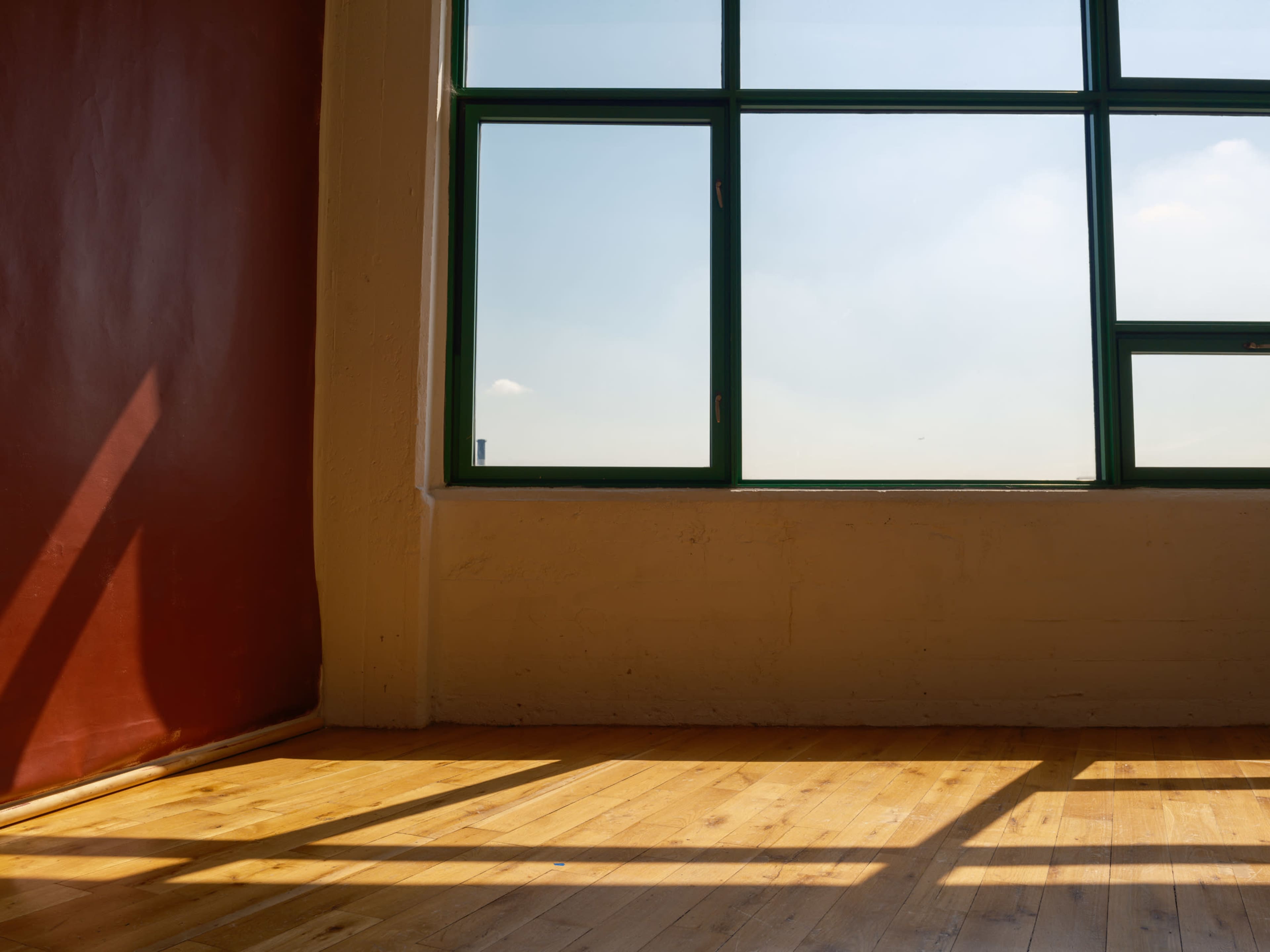 The image shows a room with a wooden floor and a large window that allows sunlight to shine in, casting shadows on the floor.
