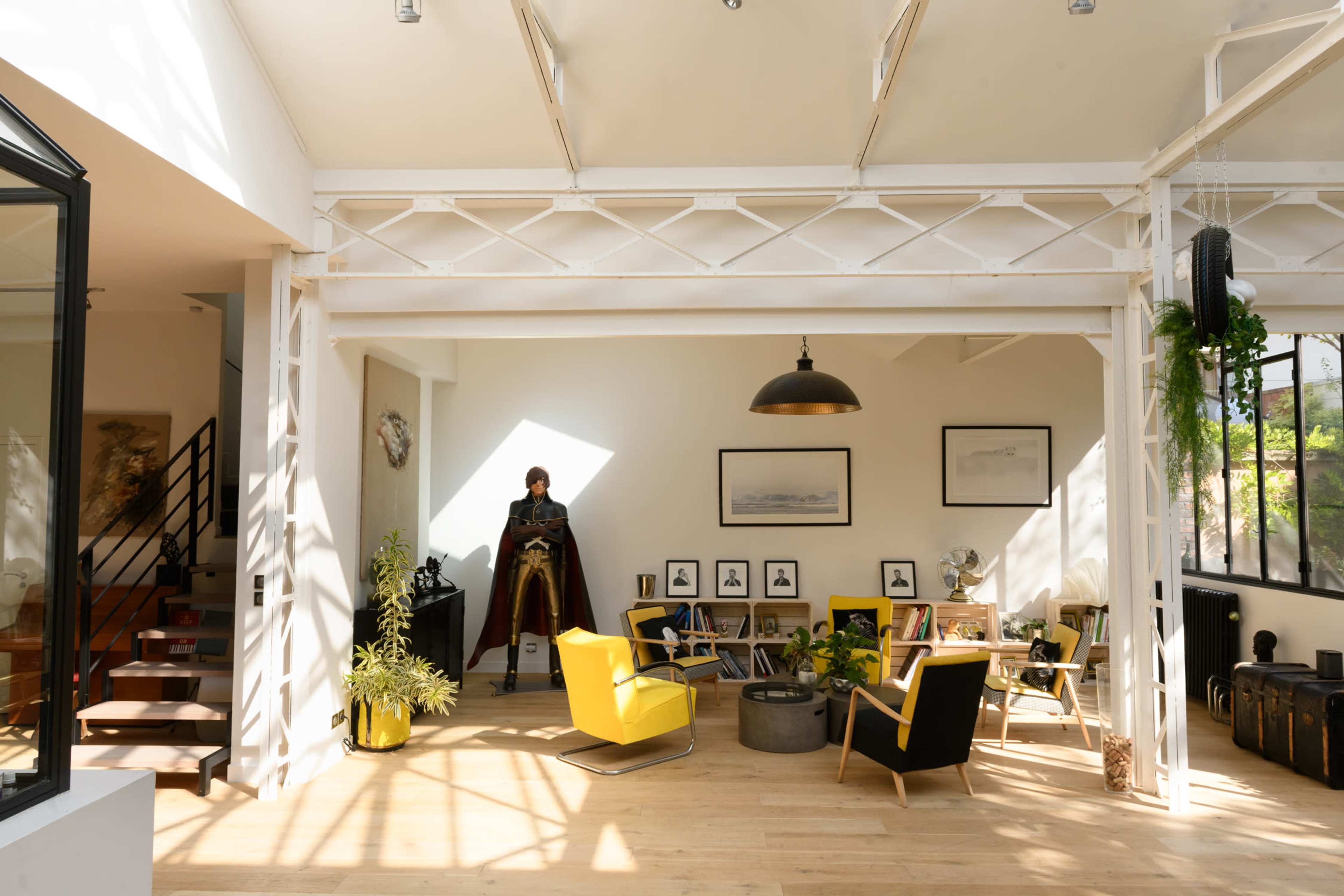 A bright, modern living room with a mix of contemporary furniture, including a yellow chair and a dark figure standing in the corner.