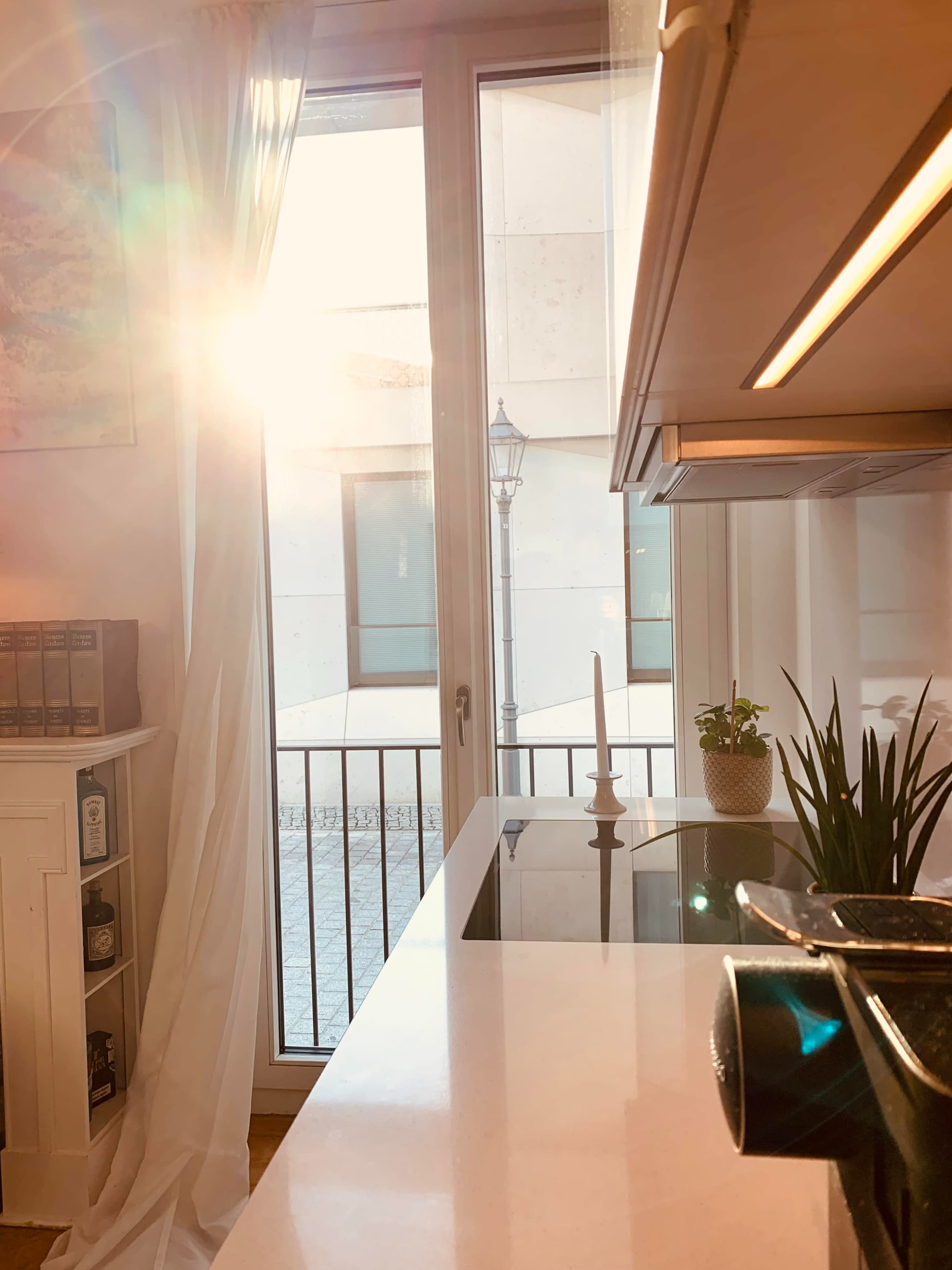 A sunbeam streams through a window, illuminating a kitchen countertop with a candle and potted plant.