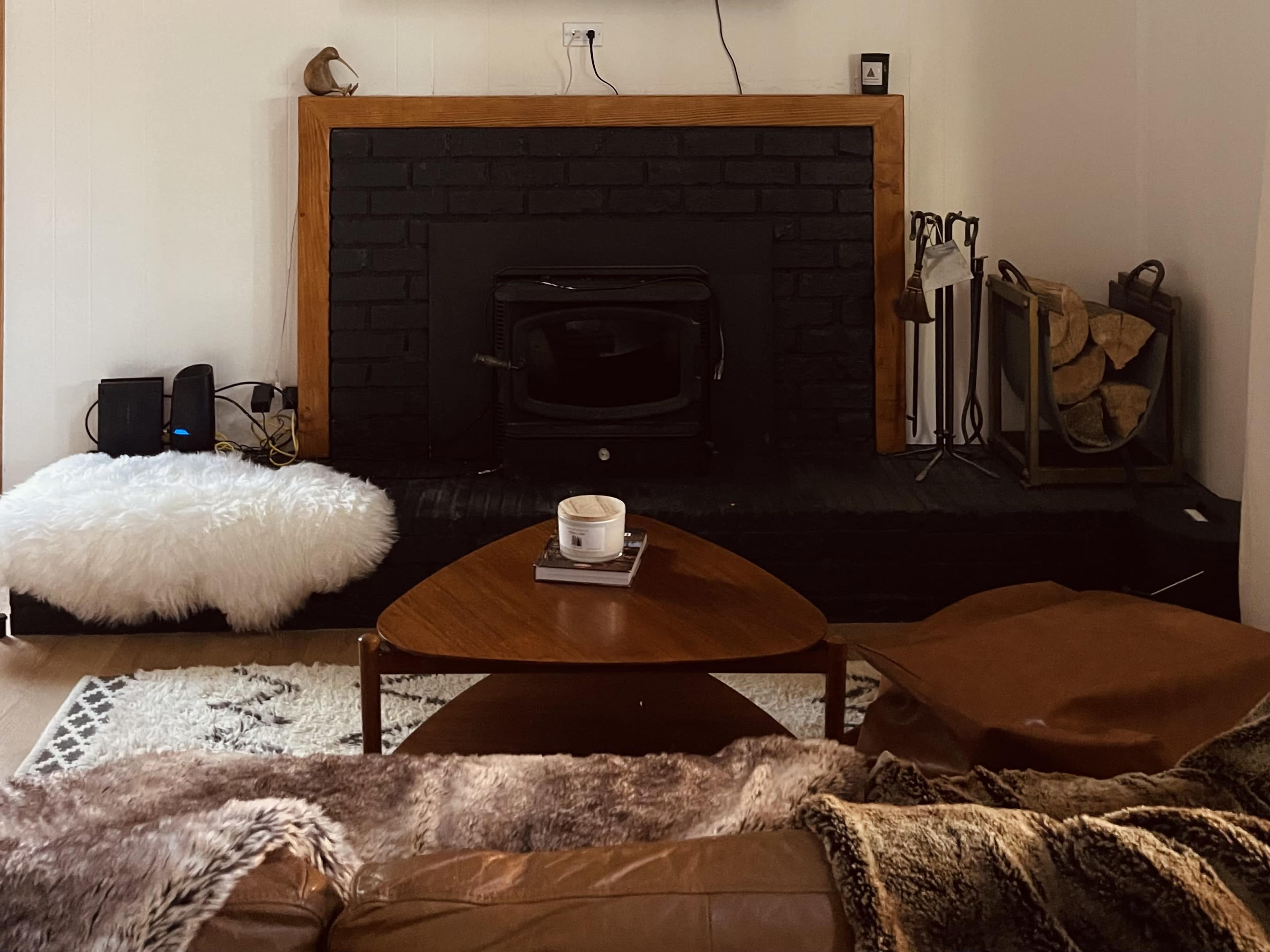 The scene features a living room with a black fireplace, a wooden mantel, a coffee table in front, and a sofa covered with a fur throw.