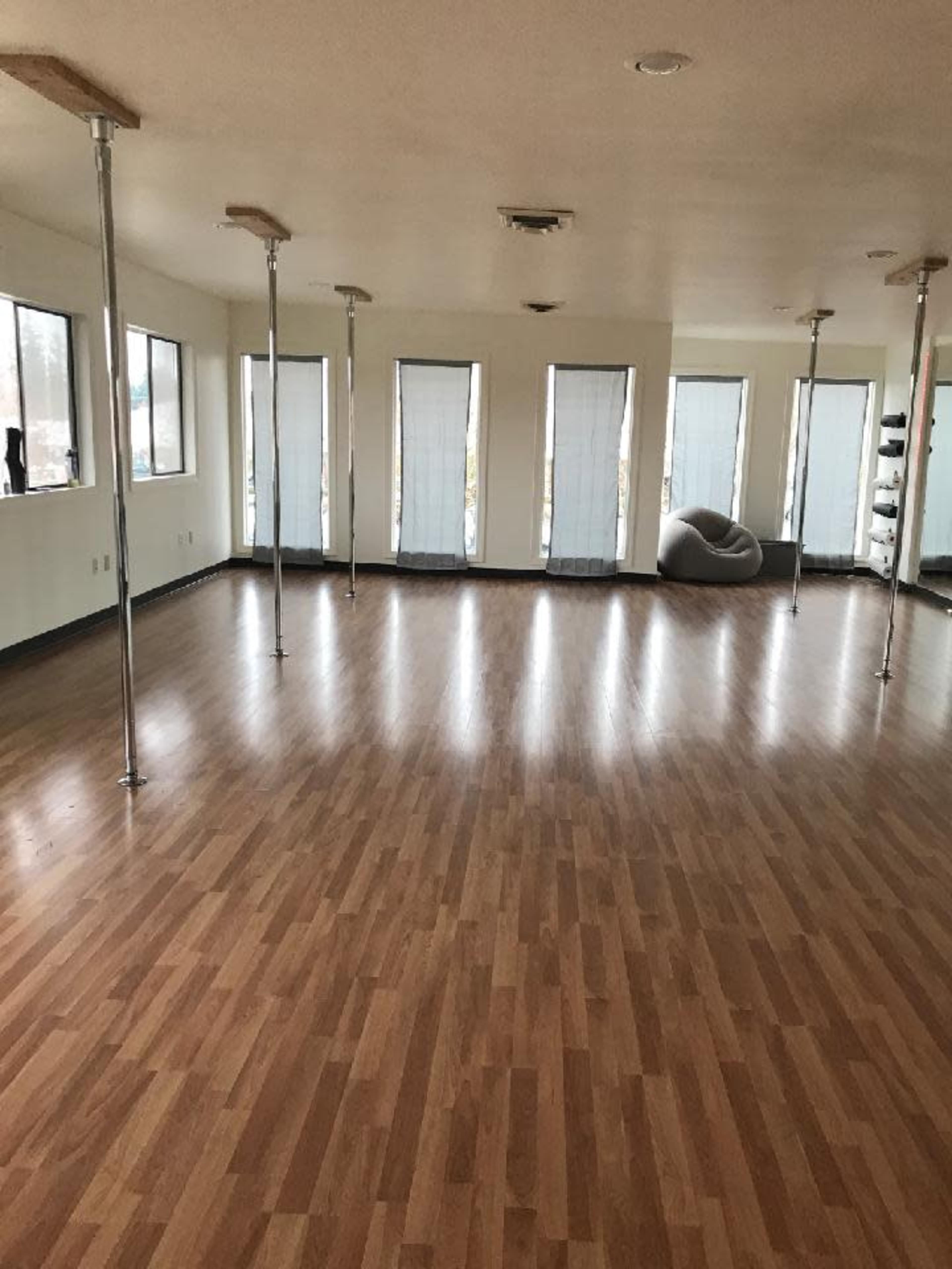 An empty room with wooden floors, large windows, and several poles installed along the perimeter.