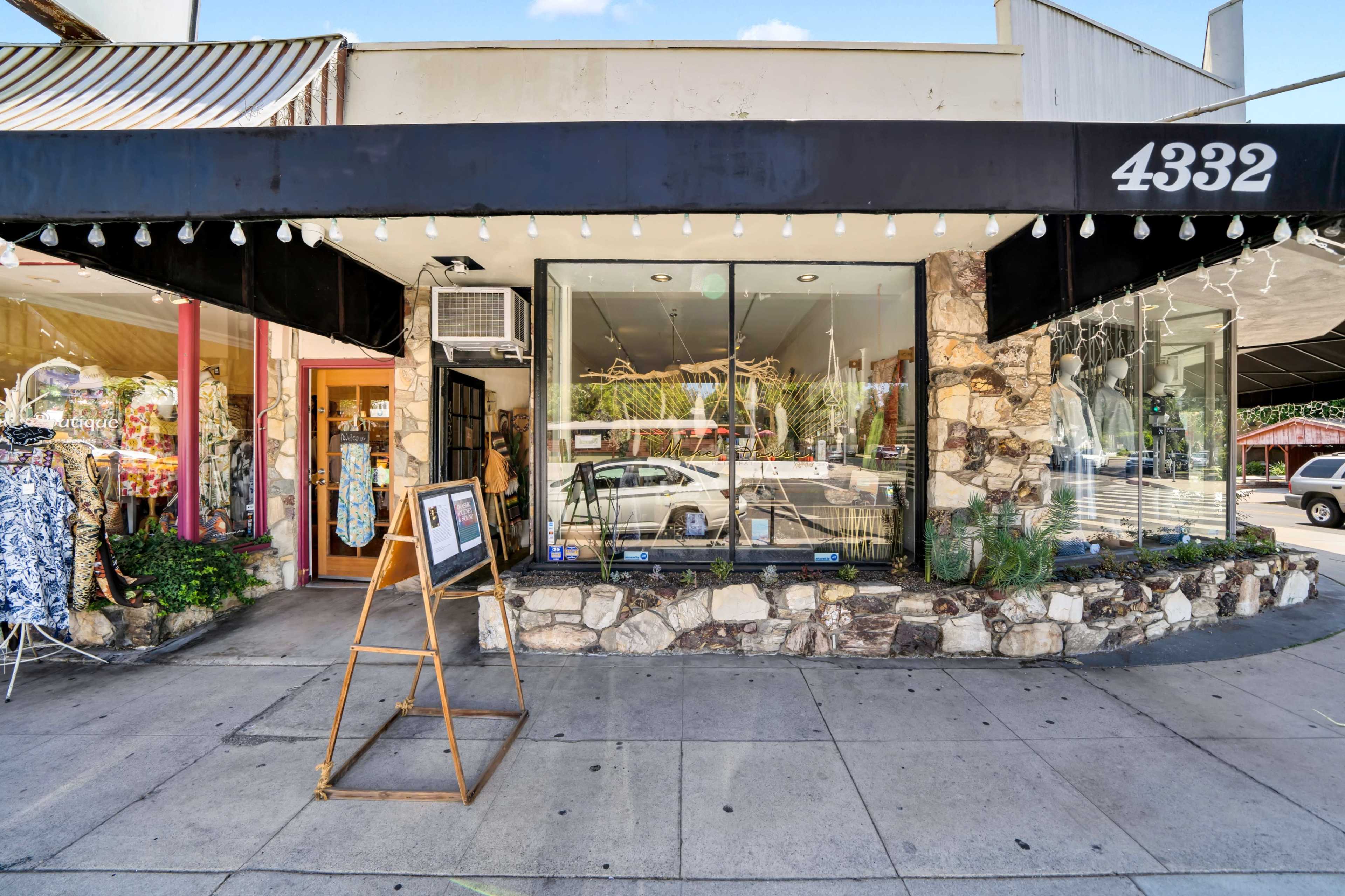 The storefront features large windows displaying various clothing items, a wooden signboard in front, and a stone facade.